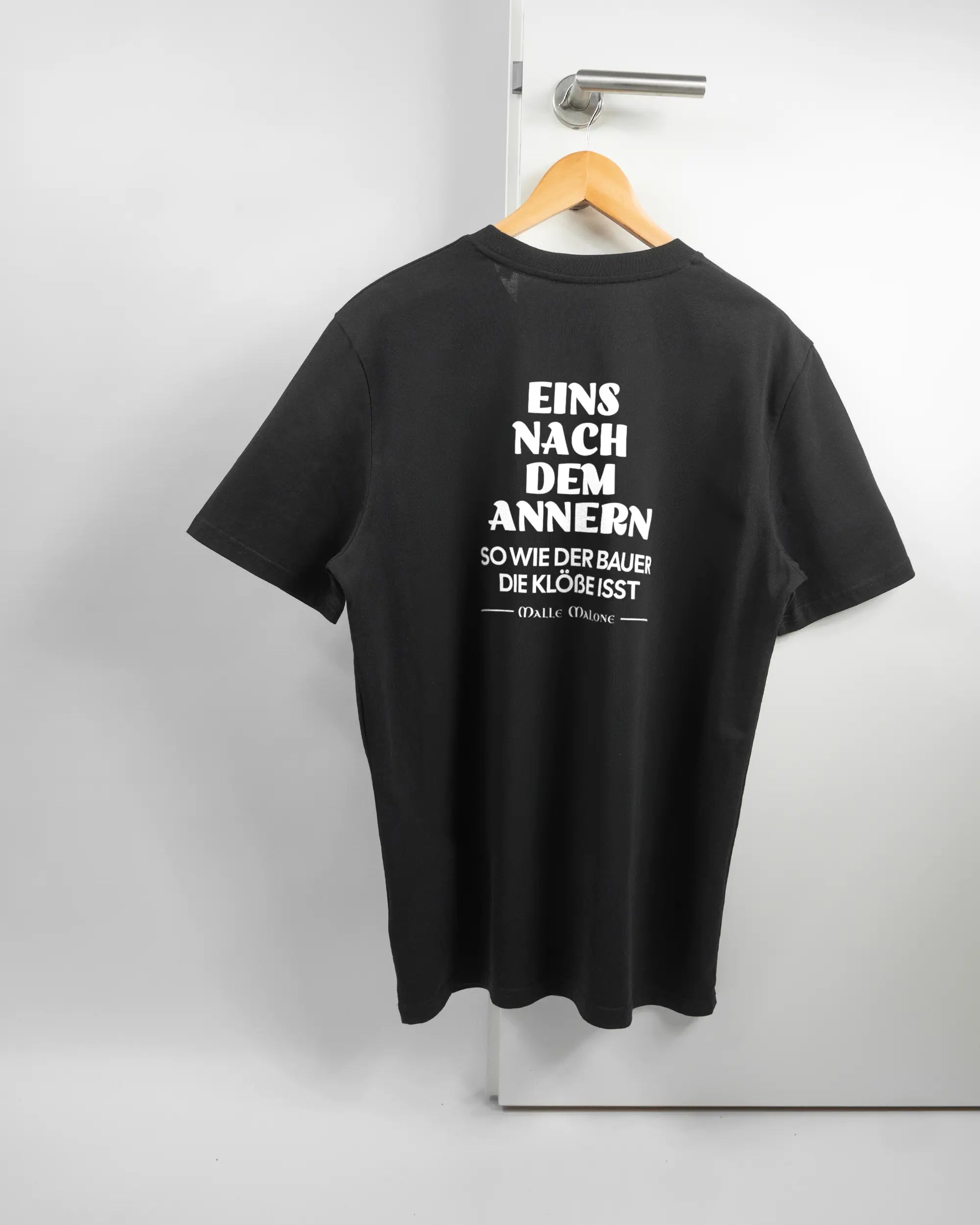 Rückseite des Organic Unisex T-Shirt Casual von Maondo mit dem Design Eins nach dem Annern in der Farbe Black und in der Größe L auf einem Bügel an der Türklinke aufgehängt