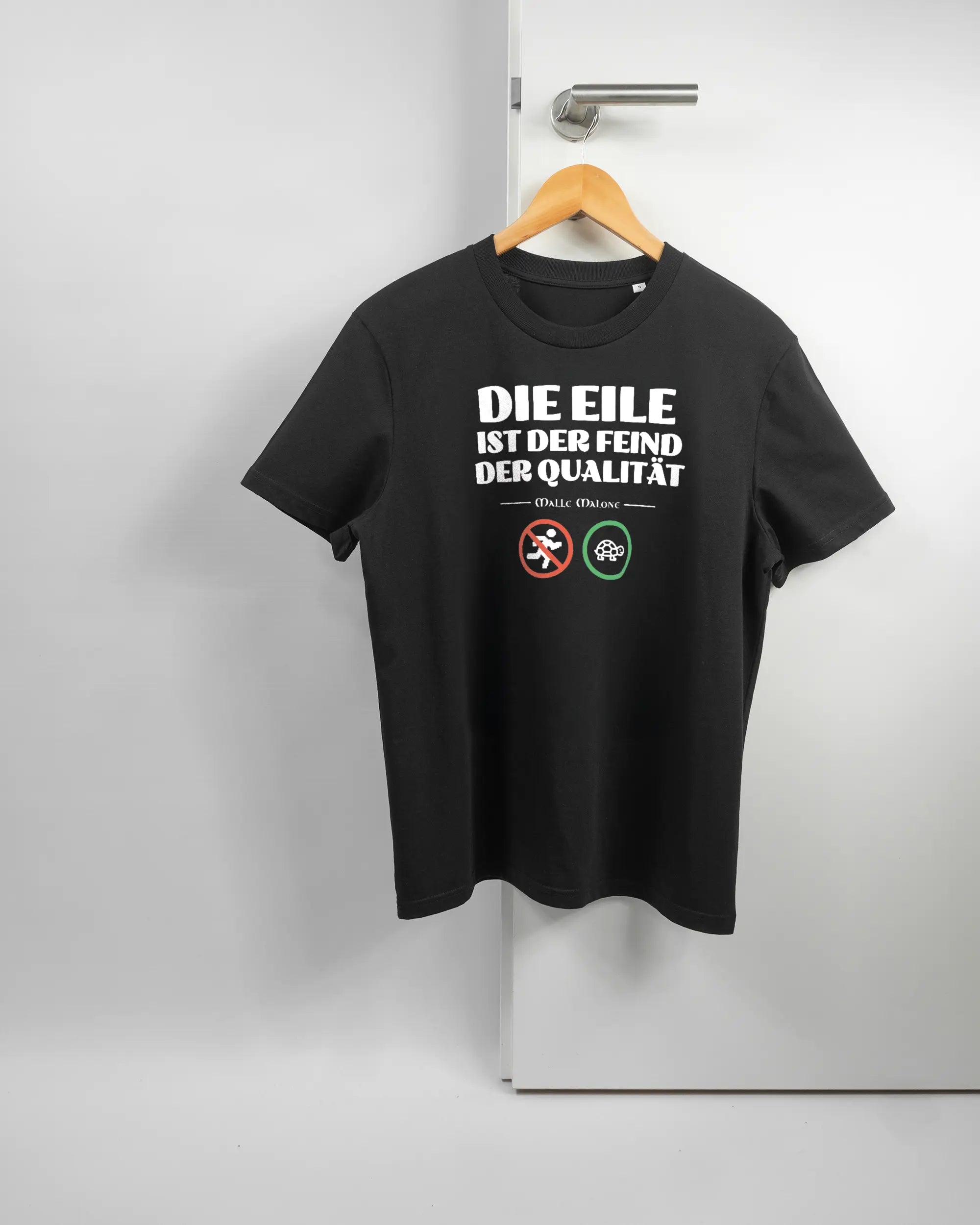 Vorderseite des Organic Unisex T-Shirt Casual von Maondo mit dem Design Keine Eile in der Farbe Black und in der Größe S auf einem Bügel an der Türklinke aufgehängt