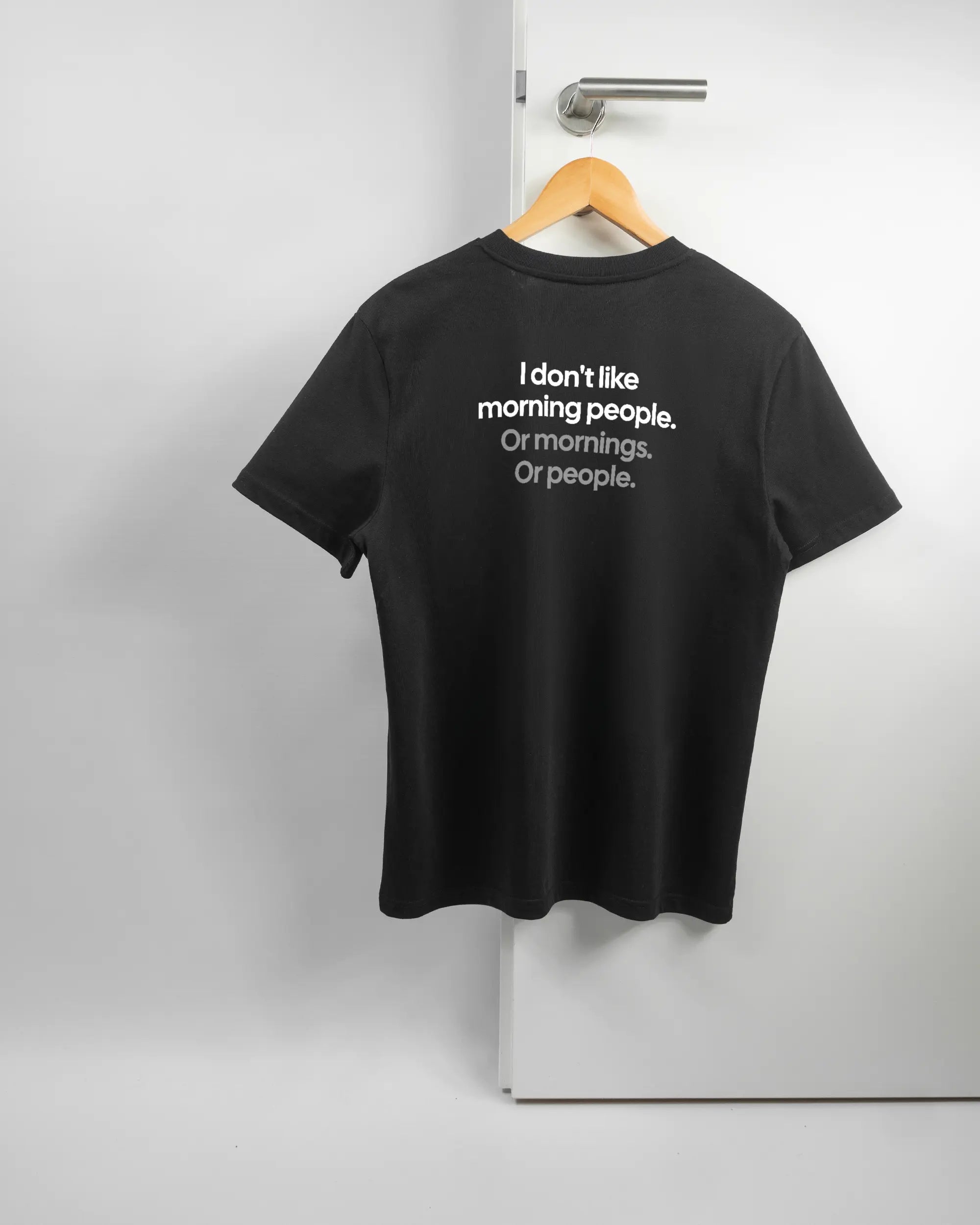 Rückseite des Organic Unisex T-Shirt Casual von Maondo mit dem Design Morning Person in der Farbe Black und in der Größe S auf einem Bügel an der Türklinke aufgehängt