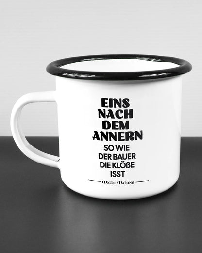 Titelbild, das die linke Seite der beidseitig bedruckten Emailletasse von Maondo mit dem Design Eins nach dem Annern in der Farbe White-Black auf einem Holztisch zeigt