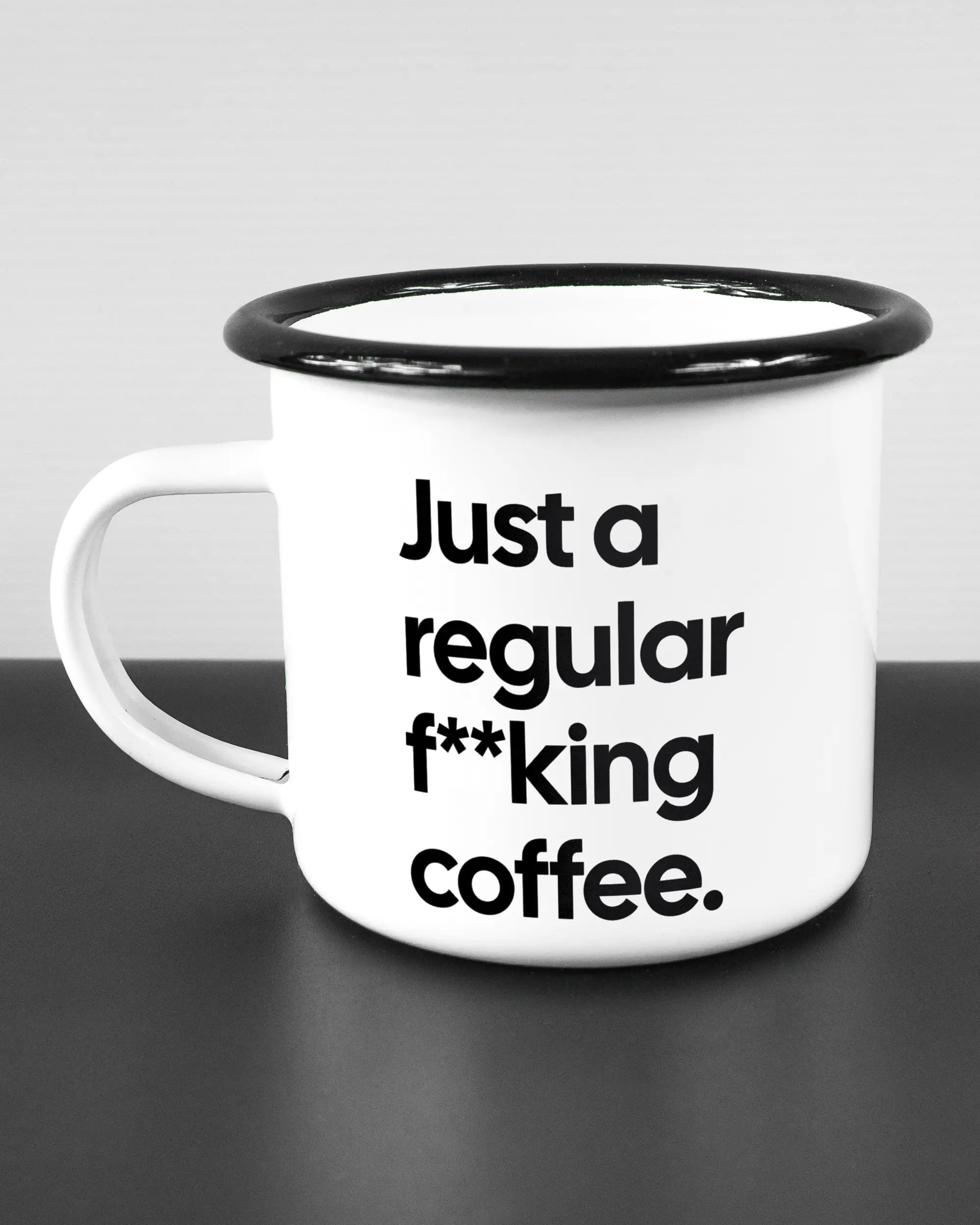 Titelbild, das die linke Seite der beidseitig bedruckten Emailletasse von Maondo mit dem Design Regular Coffee in der Farbe White-Black auf einem Holztisch zeigt