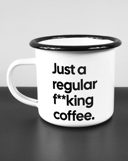 Titelbild, das die linke Seite der beidseitig bedruckten Emailletasse von Maondo mit dem Design Regular Coffee in der Farbe White-Black auf einem Holztisch zeigt