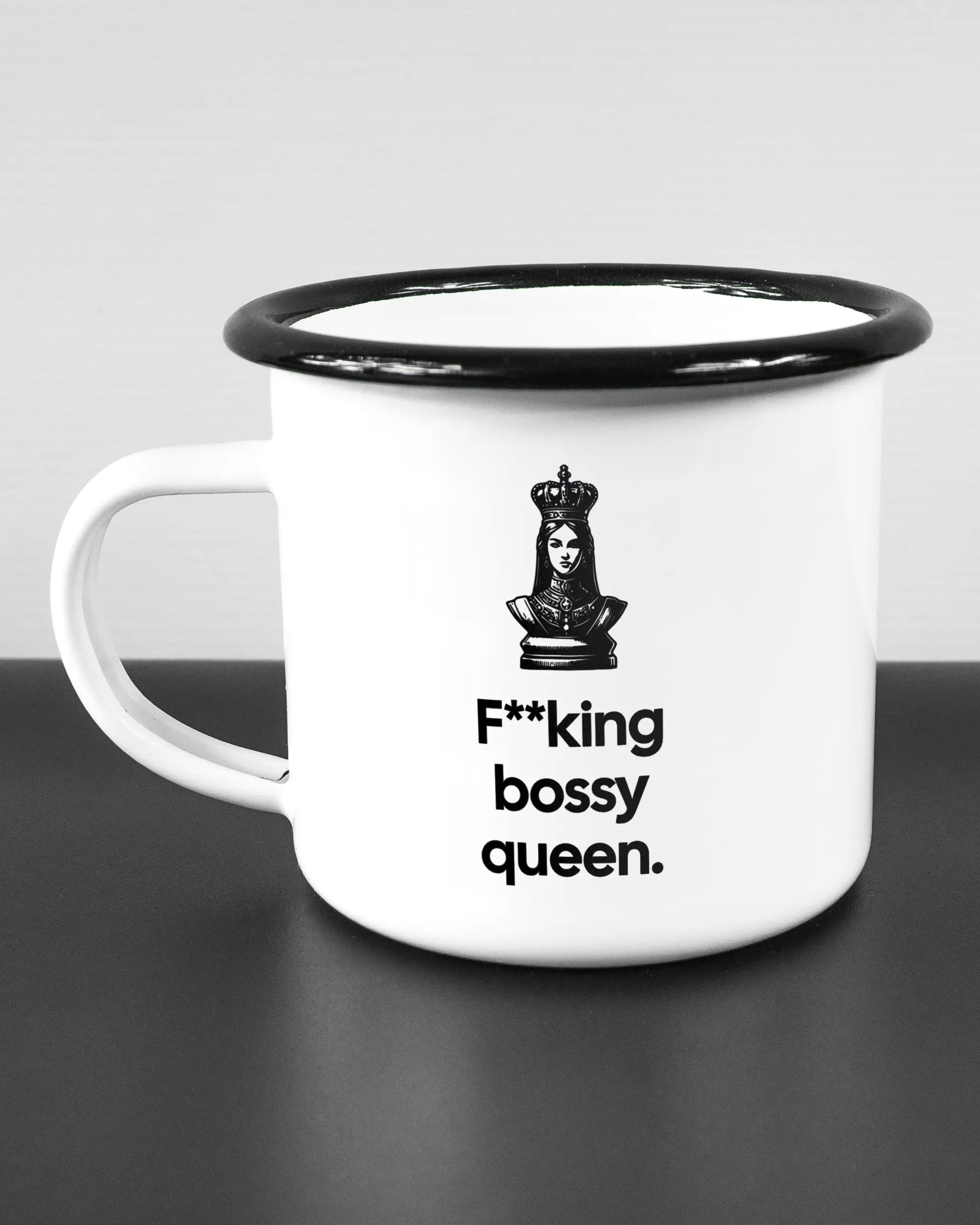 Titelbild, das die linke Seite der beidseitig bedruckten Emailletasse von Maondo mit dem Design Bossy Queen in der Farbe White-Black auf einem Holztisch zeigt