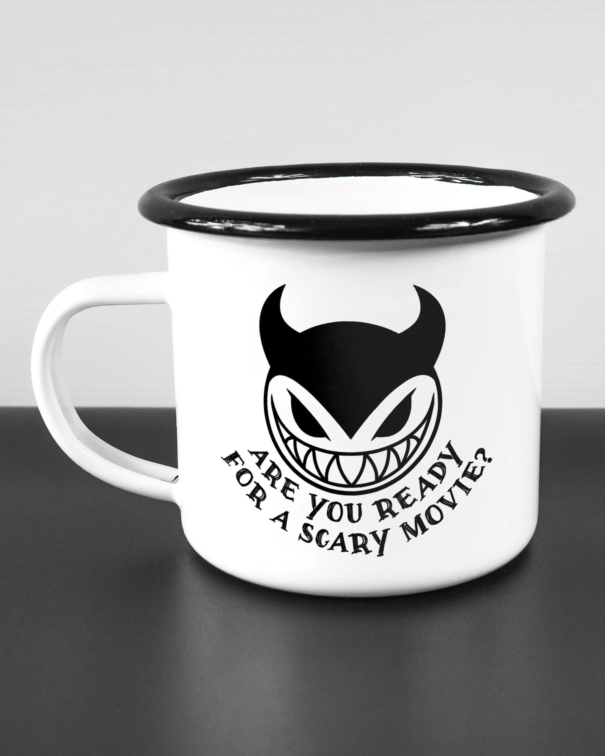 Titelbild, das die linke Seite der beidseitig bedruckten Emailletasse von Maondo mit dem Design Scary Movie in der Farbe White-Black auf einem Holztisch zeigt