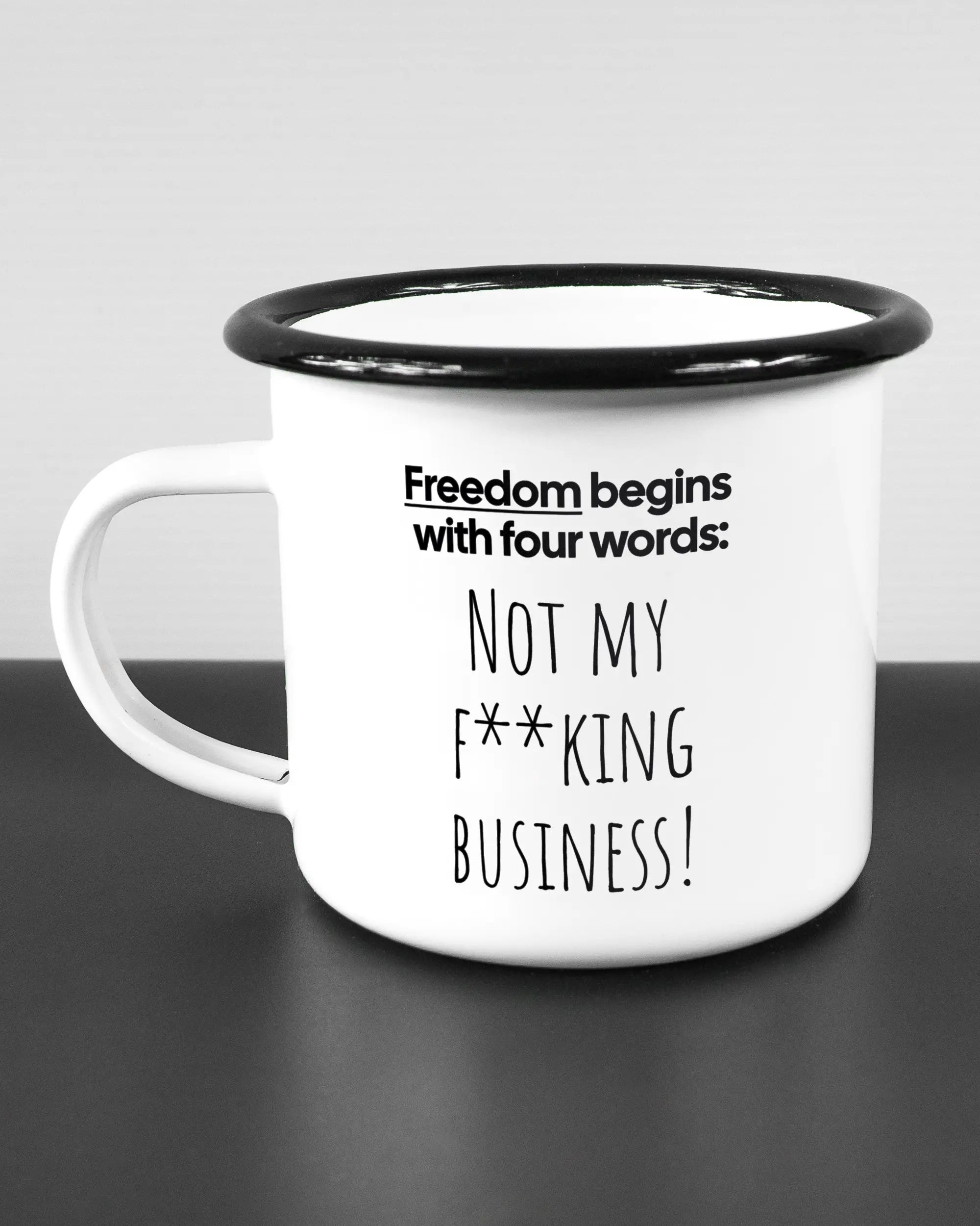 Titelbild, das die linke Seite der beidseitig bedruckten Emailletasse von Maondo mit dem Design 4 Freedom in der Farbe White-Black auf einem Holztisch zeigt