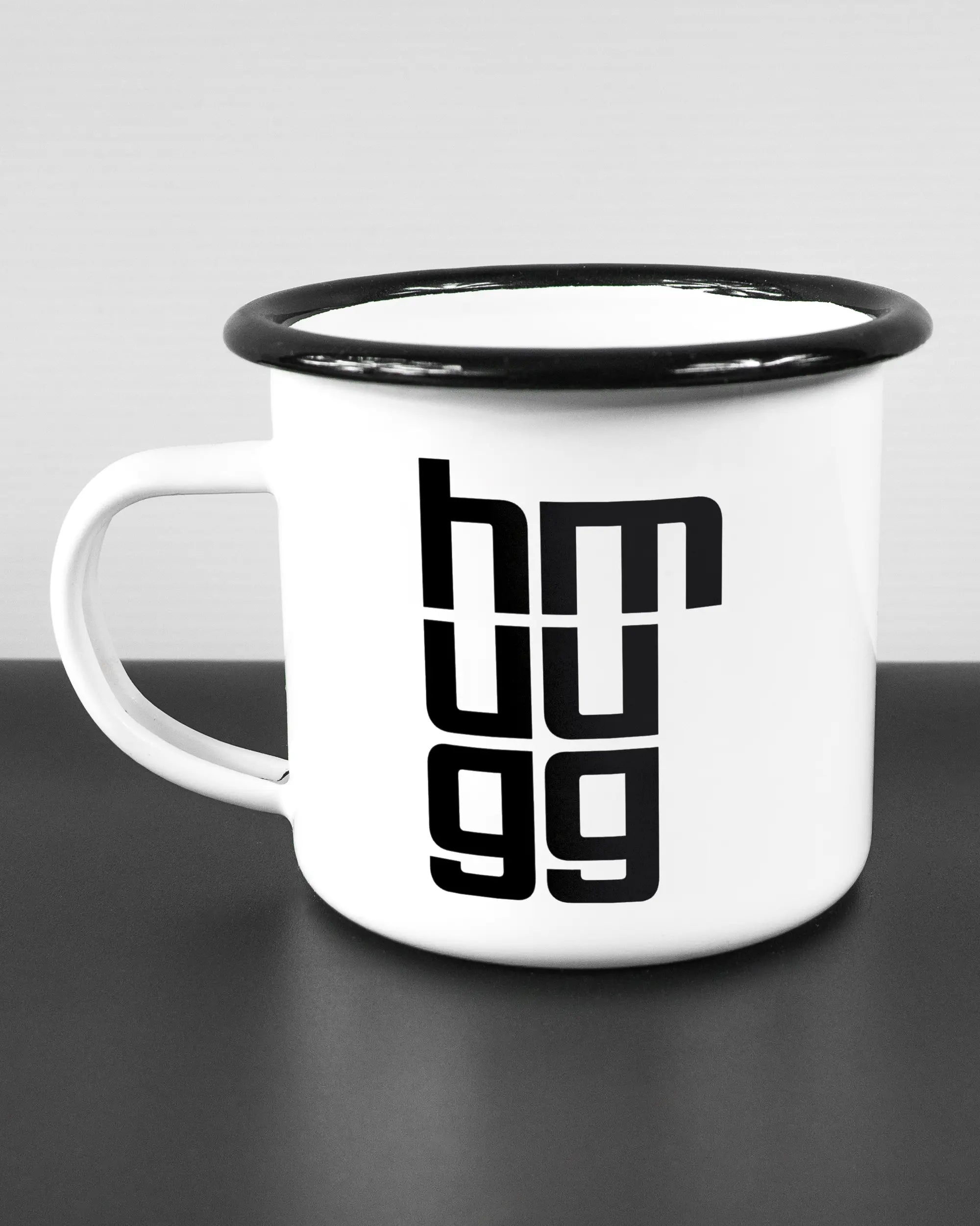 Titelbild, das die linke Seite der beidseitig bedruckten Emailletasse von Maondo mit dem Design Hug Mug in der Farbe White-Black auf einem Holztisch zeigt