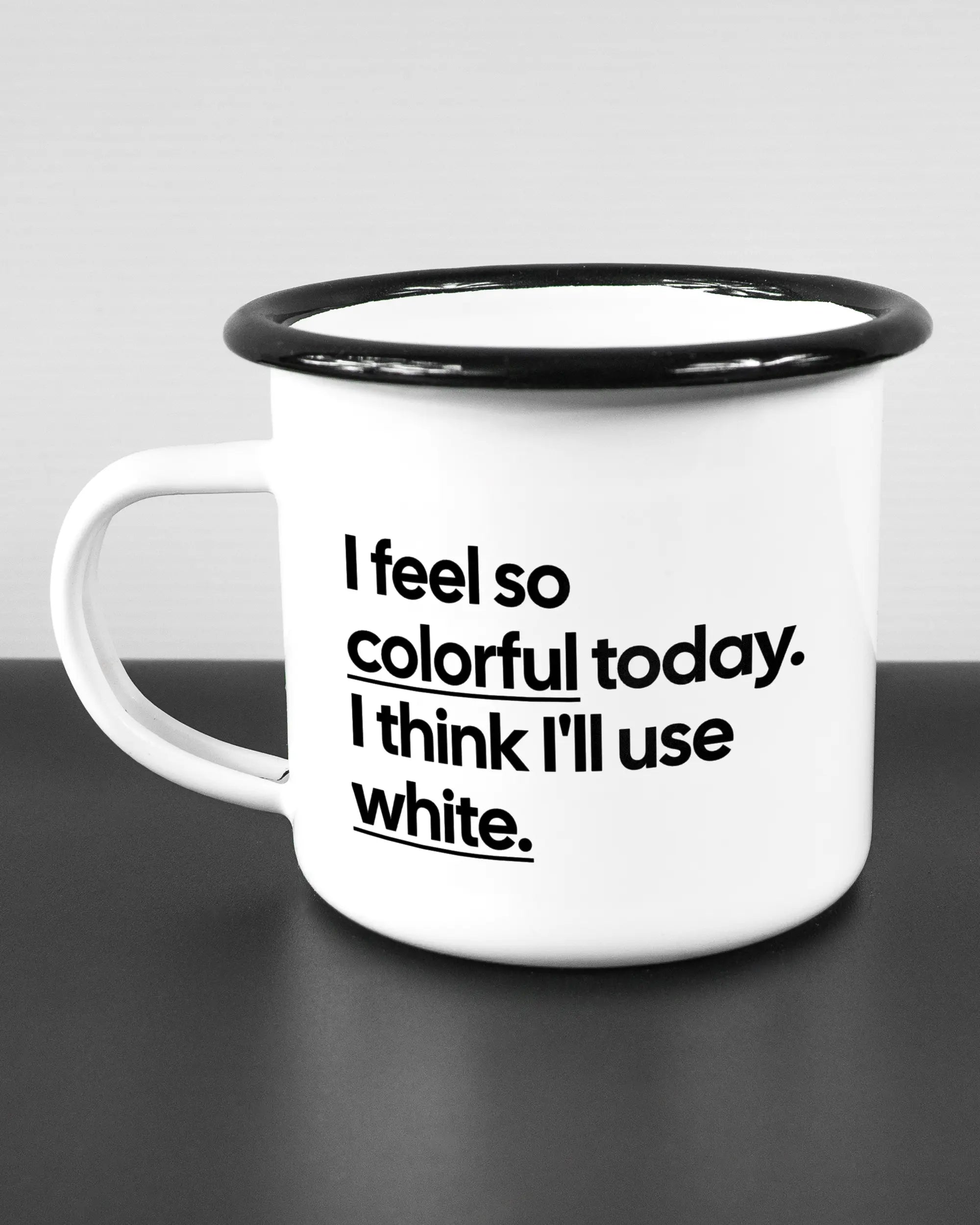 Titelbild, das die linke Seite der beidseitig bedruckten Emailletasse von Maondo mit dem Design Colorful Day in der Farbe White-Black auf einem Holztisch zeigt