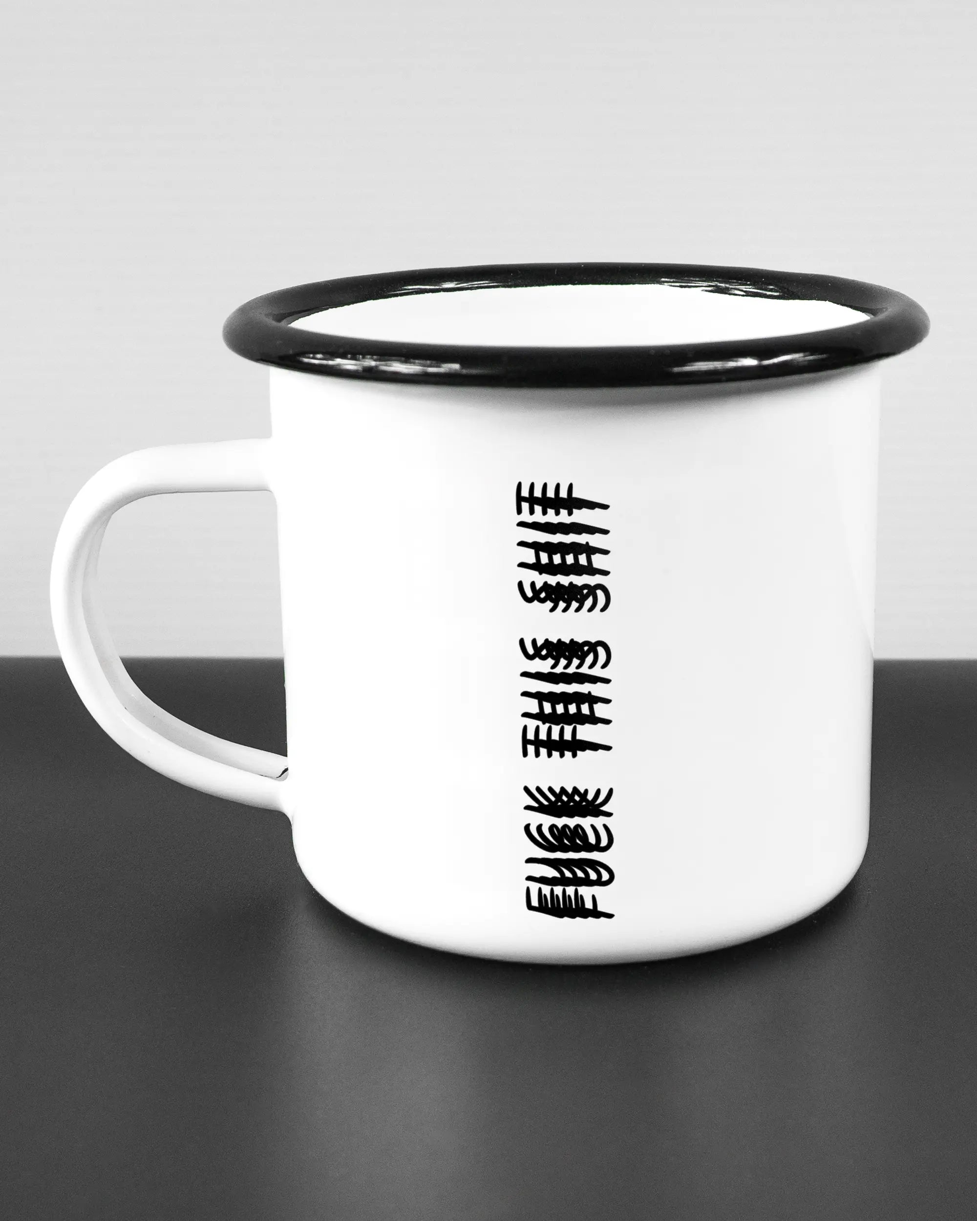 Titelbild, das die linke Seite der beidseitig bedruckten Emailletasse von Maondo mit dem Design Hidden Message in der Farbe White-Black auf einem Holztisch zeigt