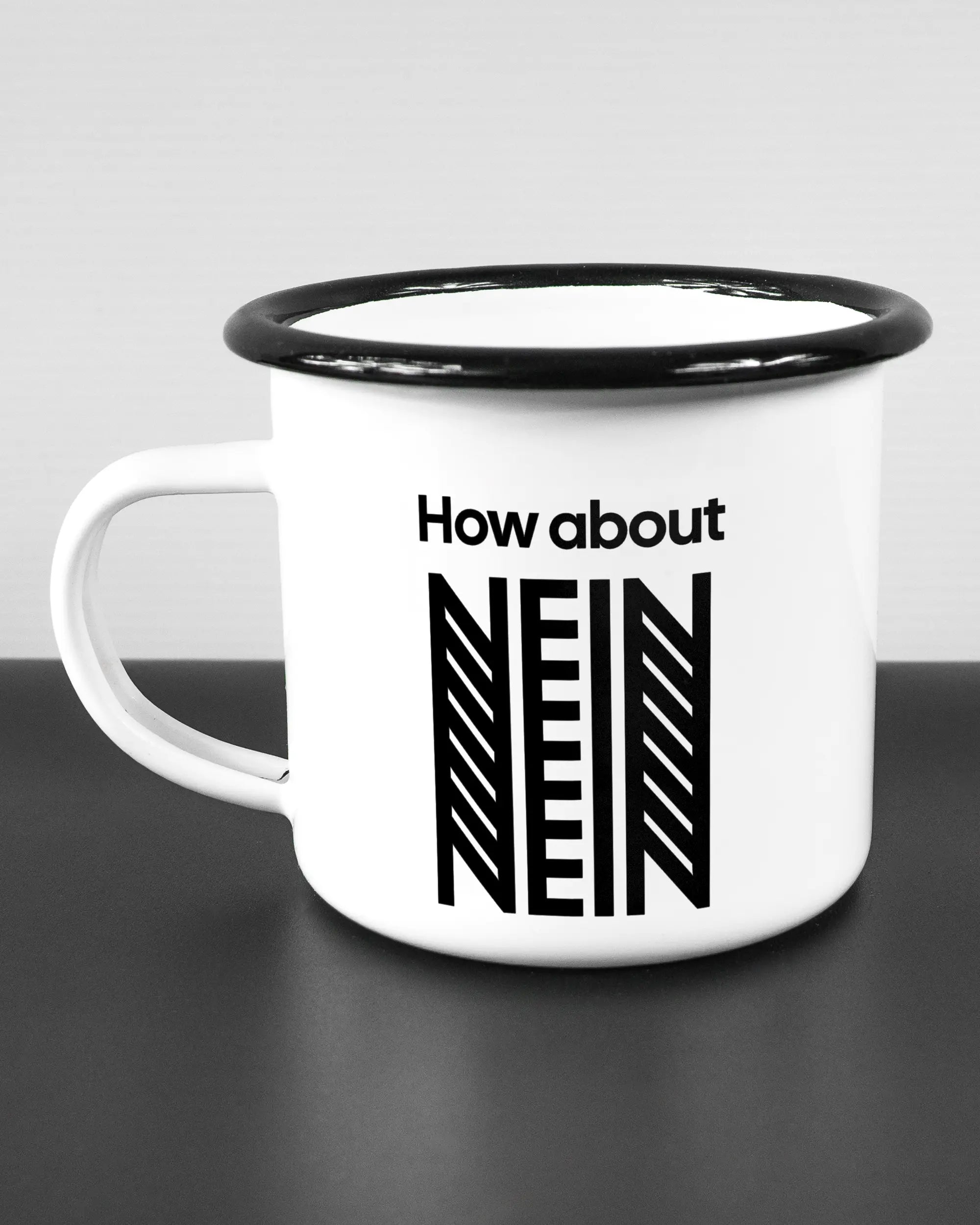 Titelbild, das die linke Seite der beidseitig bedruckten Emailletasse von Maondo mit dem Design How about nein in der Farbe White-Black auf einem Holztisch zeigt
