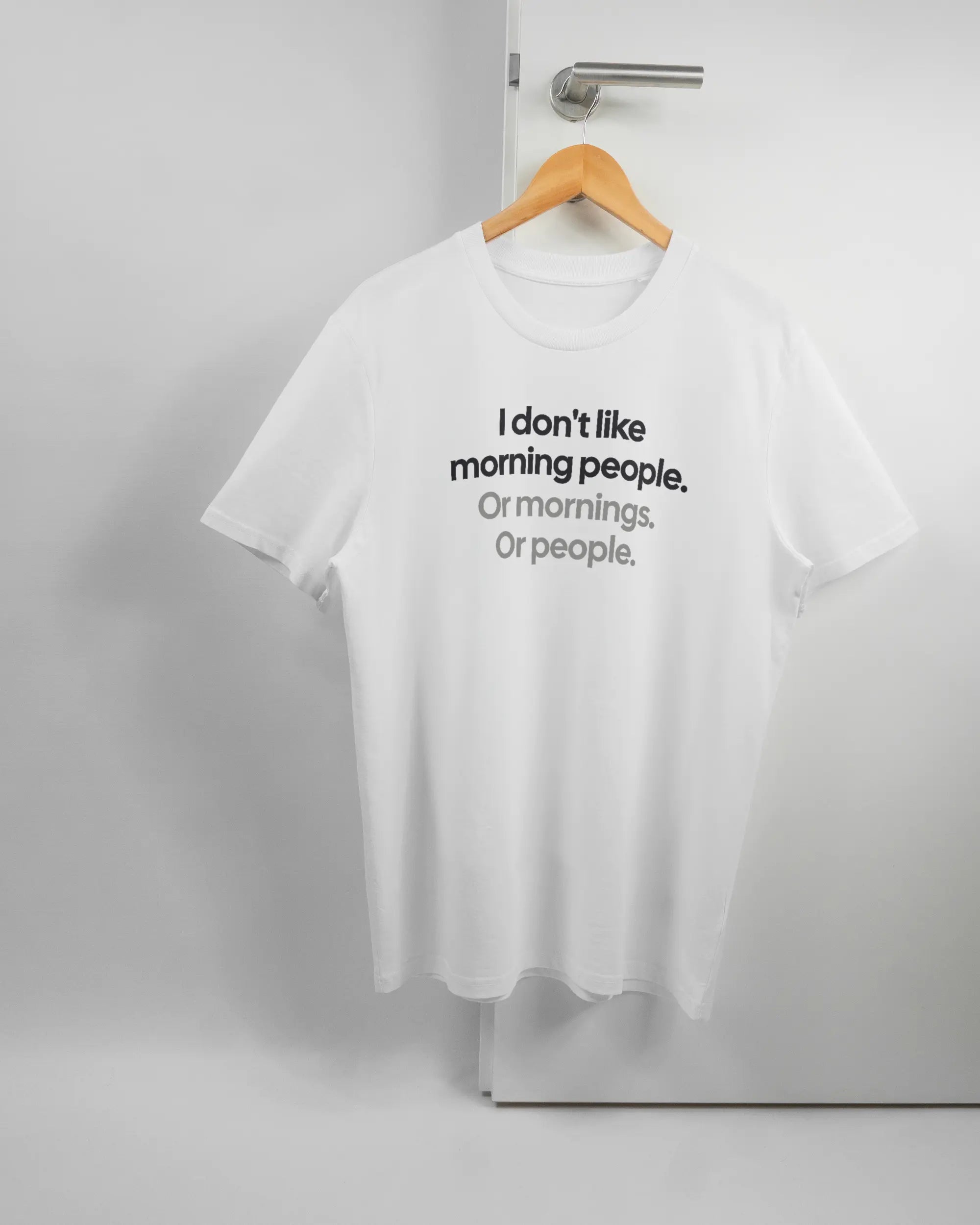 Vorderseite des Organic Unisex T-Shirt Casual von Maondo mit dem Design Morning Person in der Farbe White und in der Größe L auf einem Bügel an der Türklinke aufgehängt