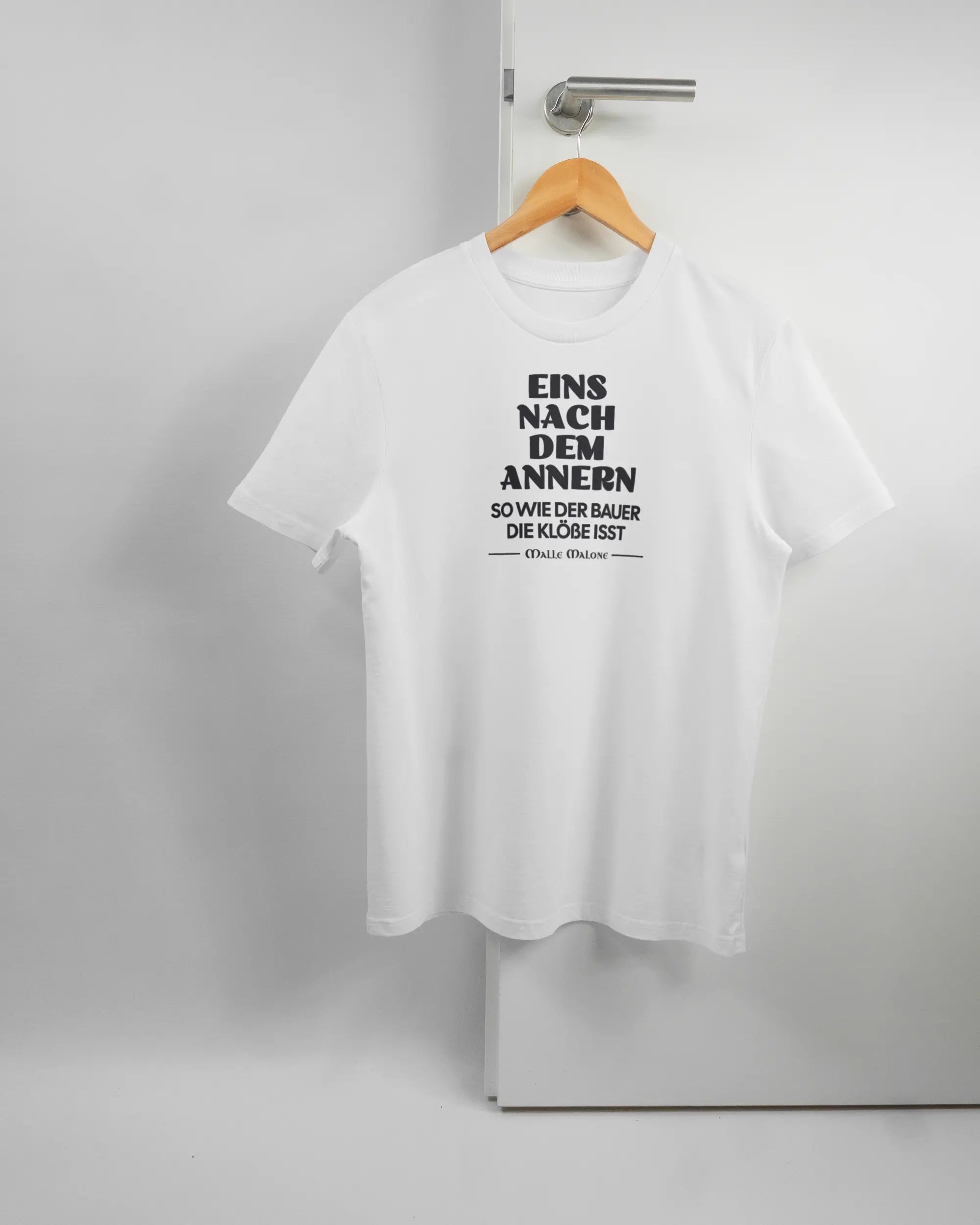 Vorderseite des Organic Unisex T-Shirt Casual von Maondo mit dem Design Eins nach dem Annern in der Farbe White und in der Größe S auf einem Bügel an der Türklinke aufgehängt