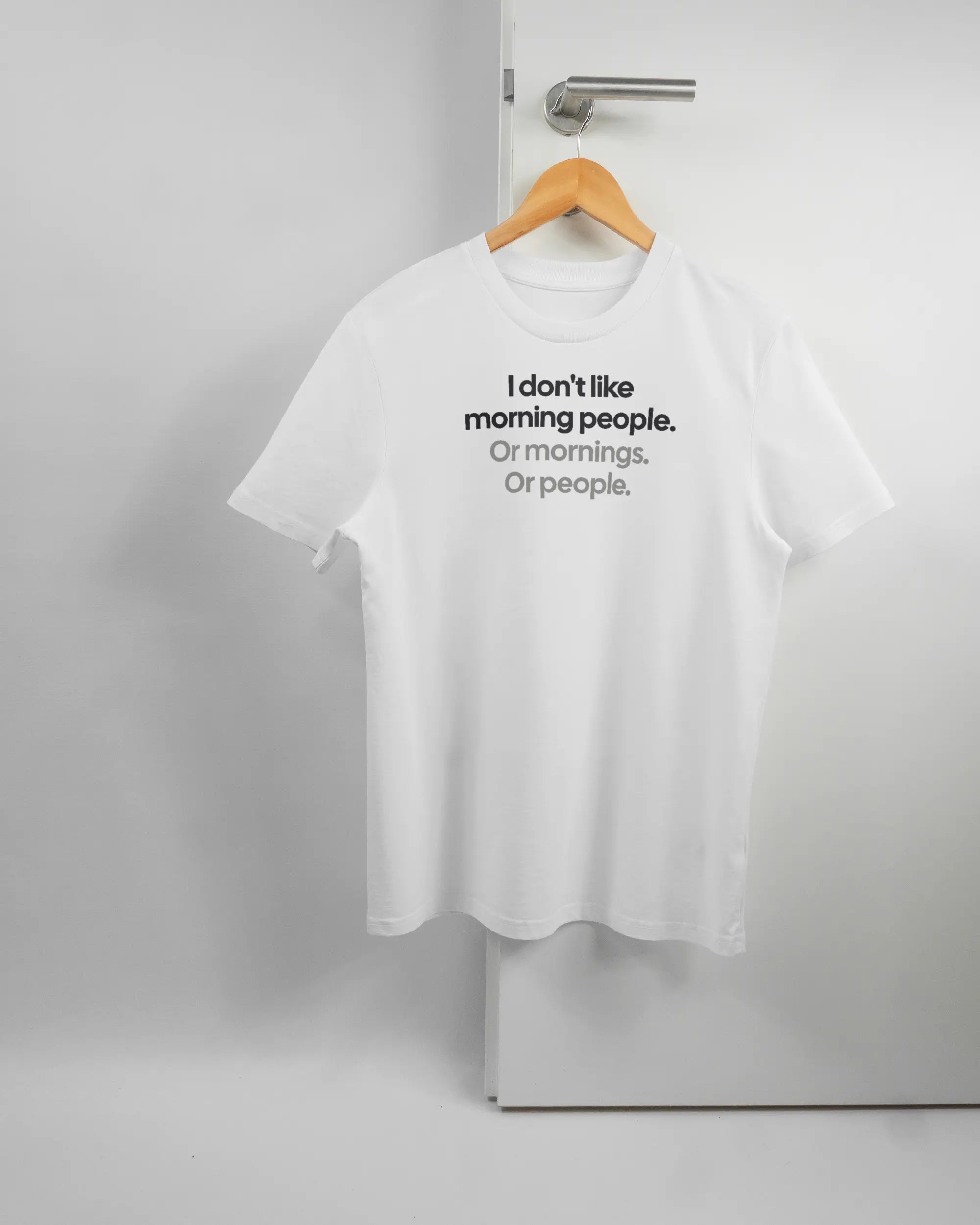 Vorderseite des Organic Unisex T-Shirt Casual von Maondo mit dem Design Morning Person in der Farbe White und in der Größe S auf einem Bügel an der Türklinke aufgehängt