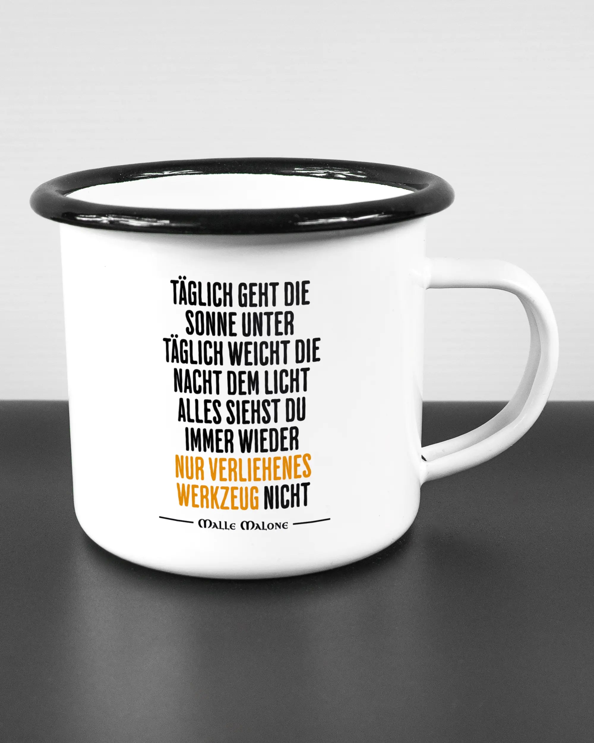 Alternativbild, das die rechte Seite der beidseitig bedruckten Emailletasse von Maondo mit dem Design Wegzeug in der Farbe White-Black auf einem Holztisch zeigt