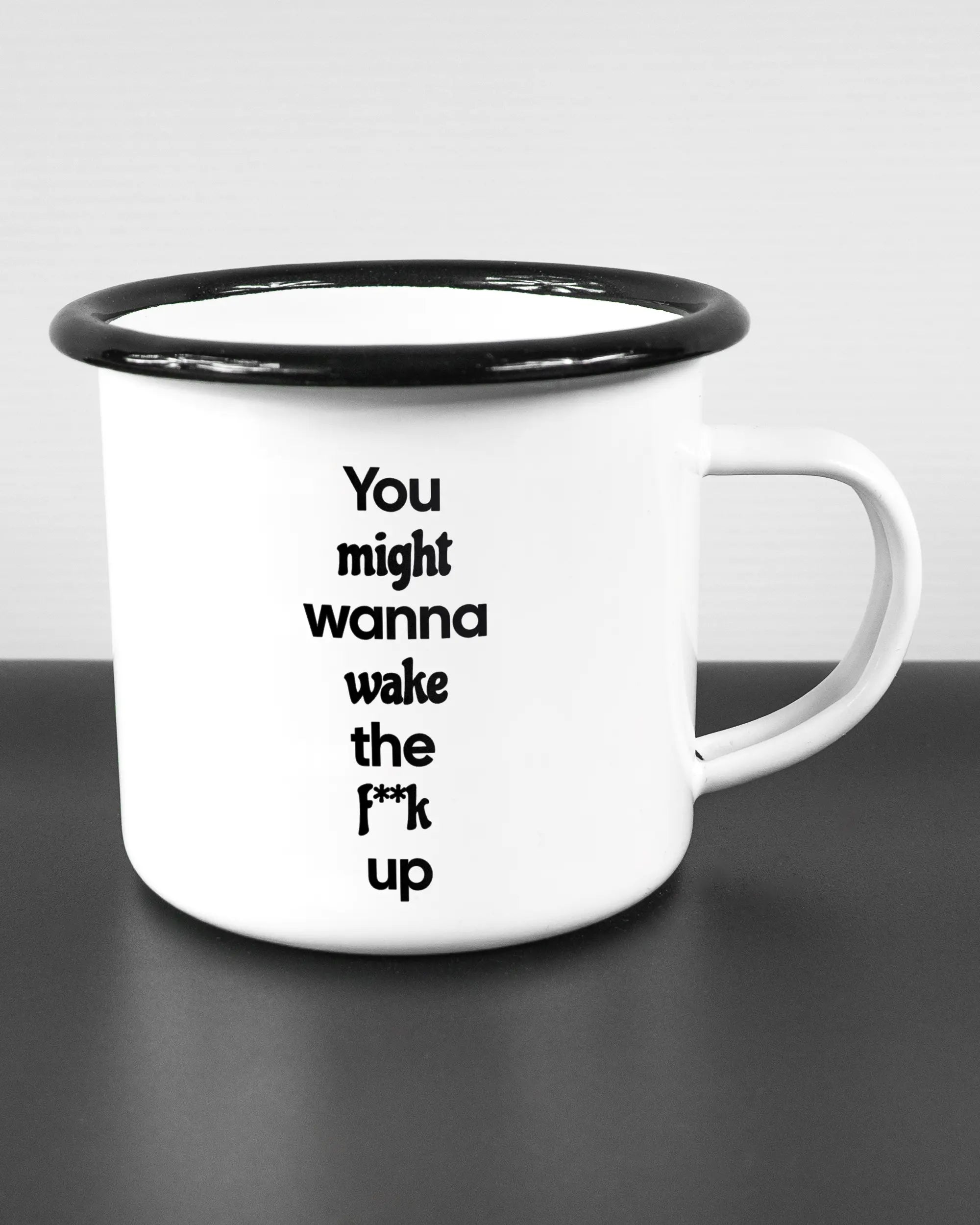 Alternativbild, das die rechte Seite der beidseitig bedruckten Emailletasse von Maondo mit dem Design Wanna Wake in der Farbe White-Black auf einem Holztisch zeigt