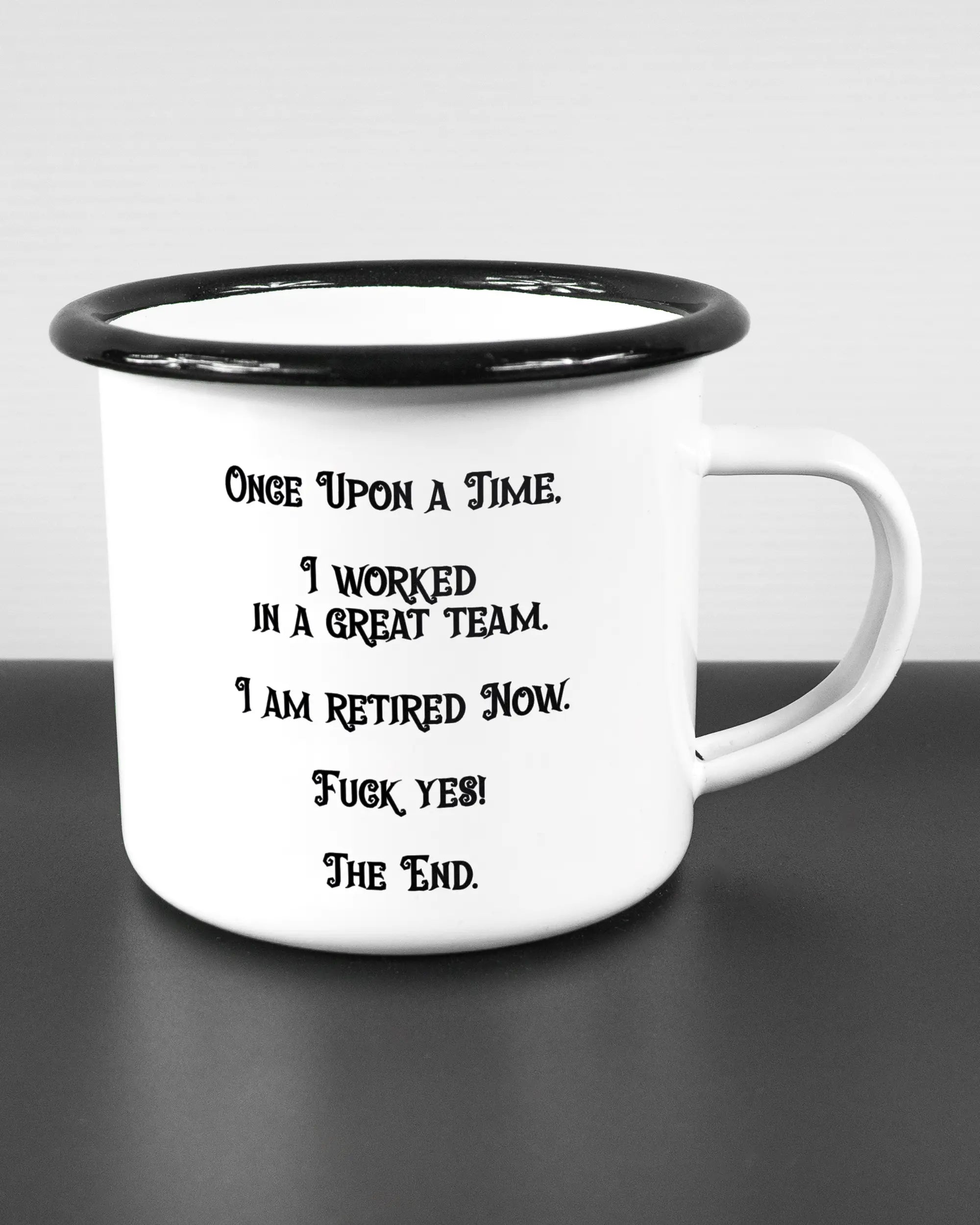 Alternativbild, das die rechte Seite der beidseitig bedruckten Emailletasse von Maondo mit dem Design Finally Retired in der Farbe White-Black auf einem Holztisch zeigt