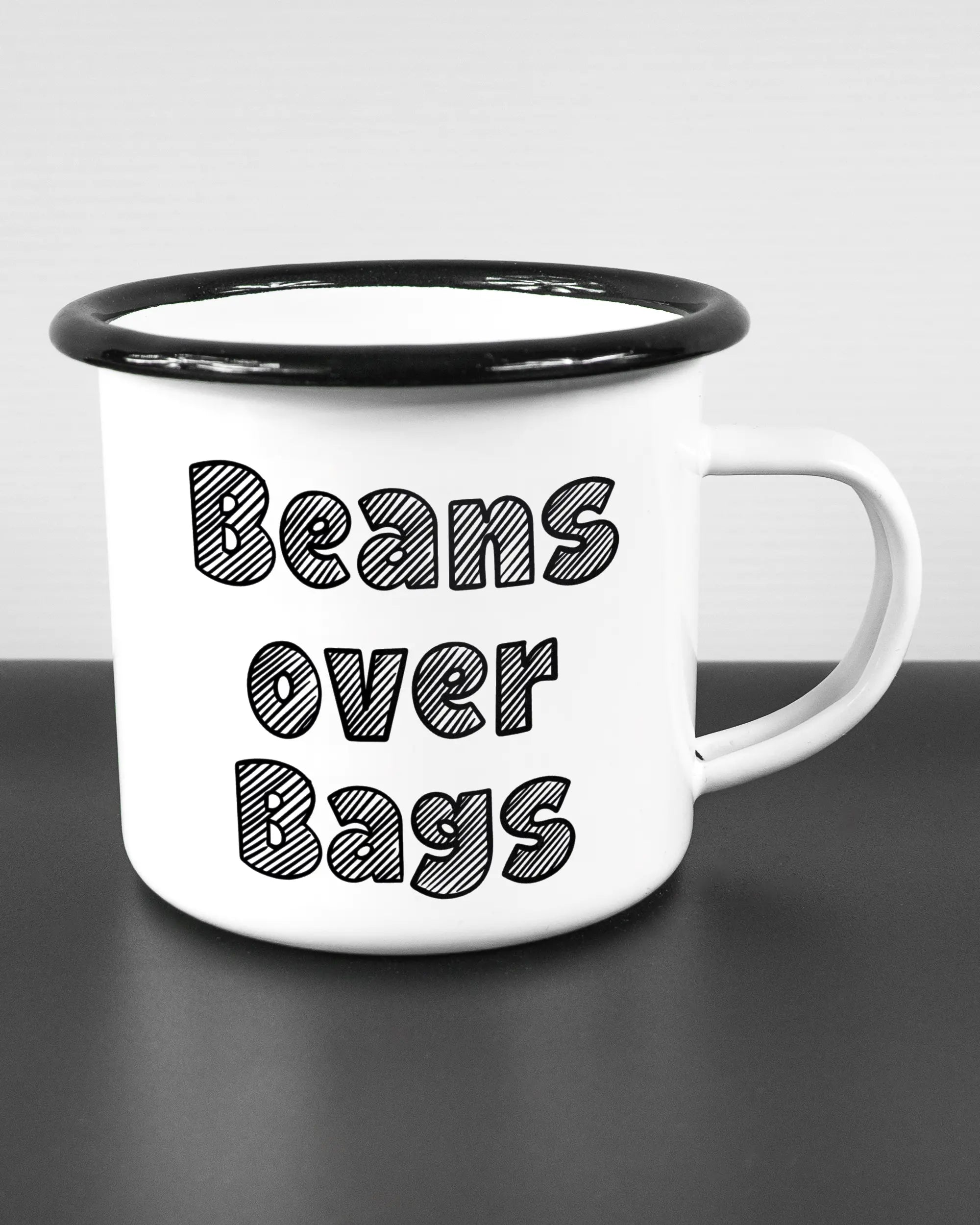 Alternativbild, das die rechte Seite der beidseitig bedruckten Emailletasse von Maondo mit dem Design Beans over Bags in der Farbe White-Black auf einem Holztisch zeigt