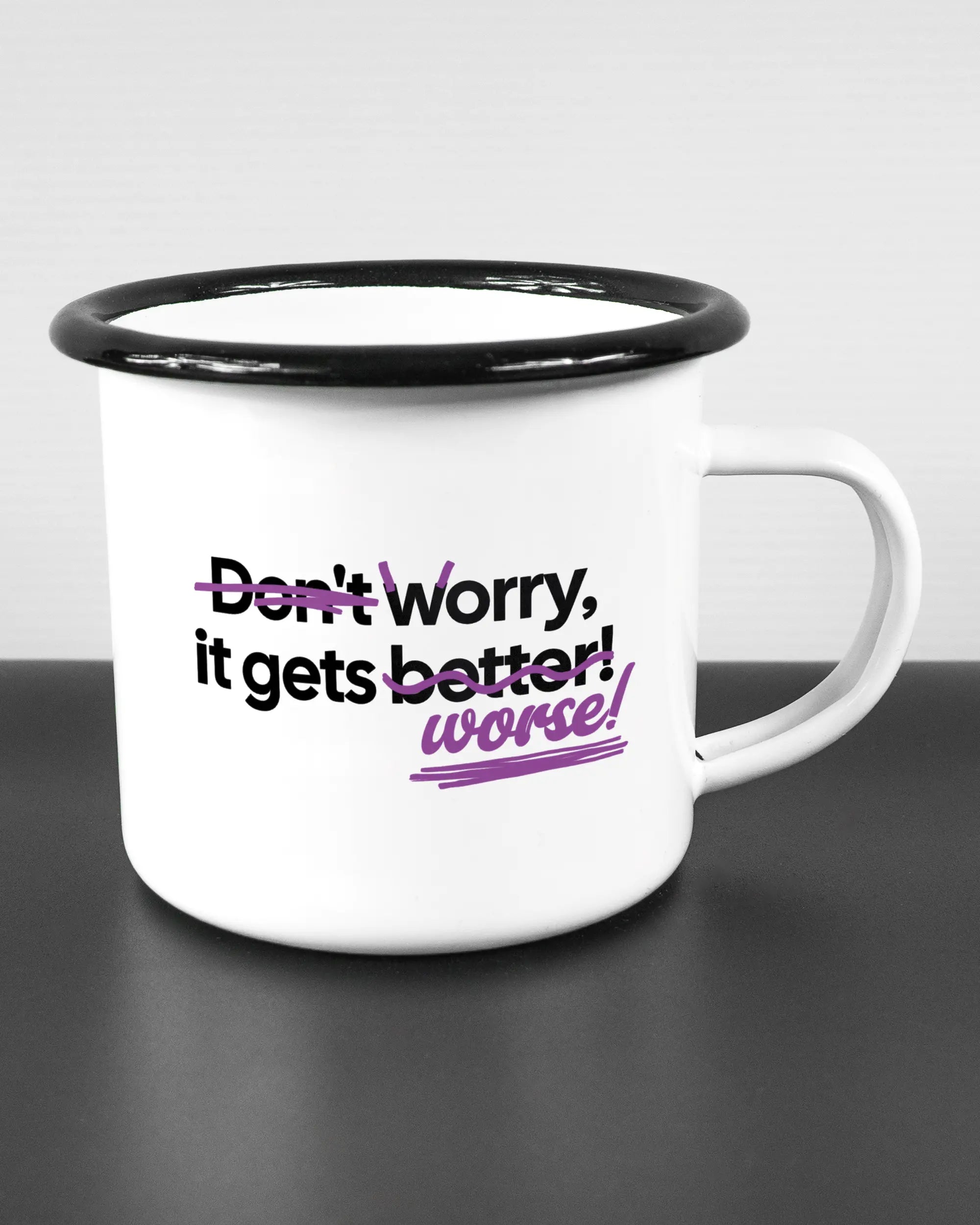 Alternativbild, das die rechte Seite der beidseitig bedruckten Emailletasse von Maondo mit dem Design Worry Worse in der Farbe White-Black auf einem Holztisch zeigt