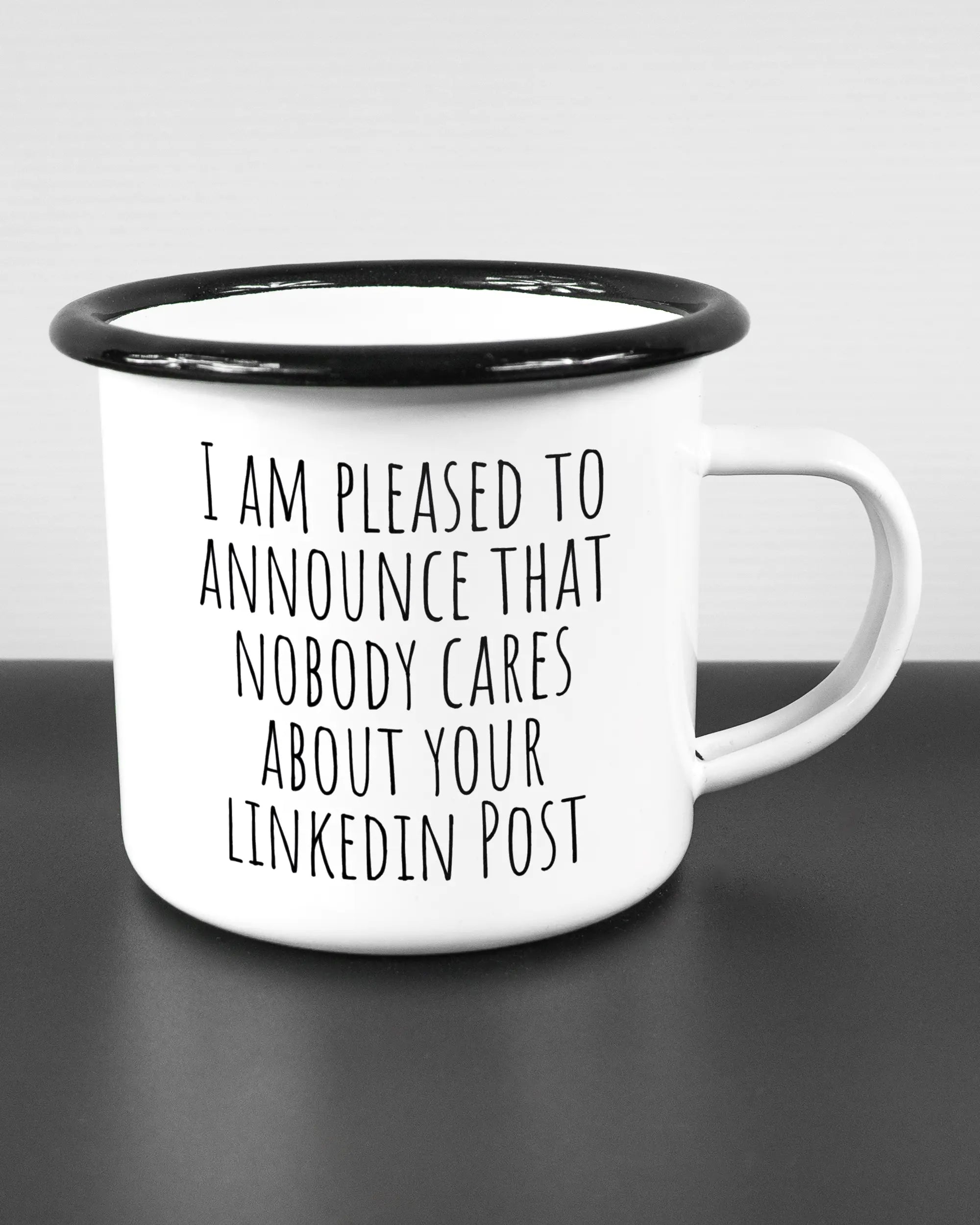 Alternativbild, das die rechte Seite der beidseitig bedruckten Emailletasse von Maondo mit dem Design Please Unannounce in der Farbe White-Black auf einem Holztisch zeigt