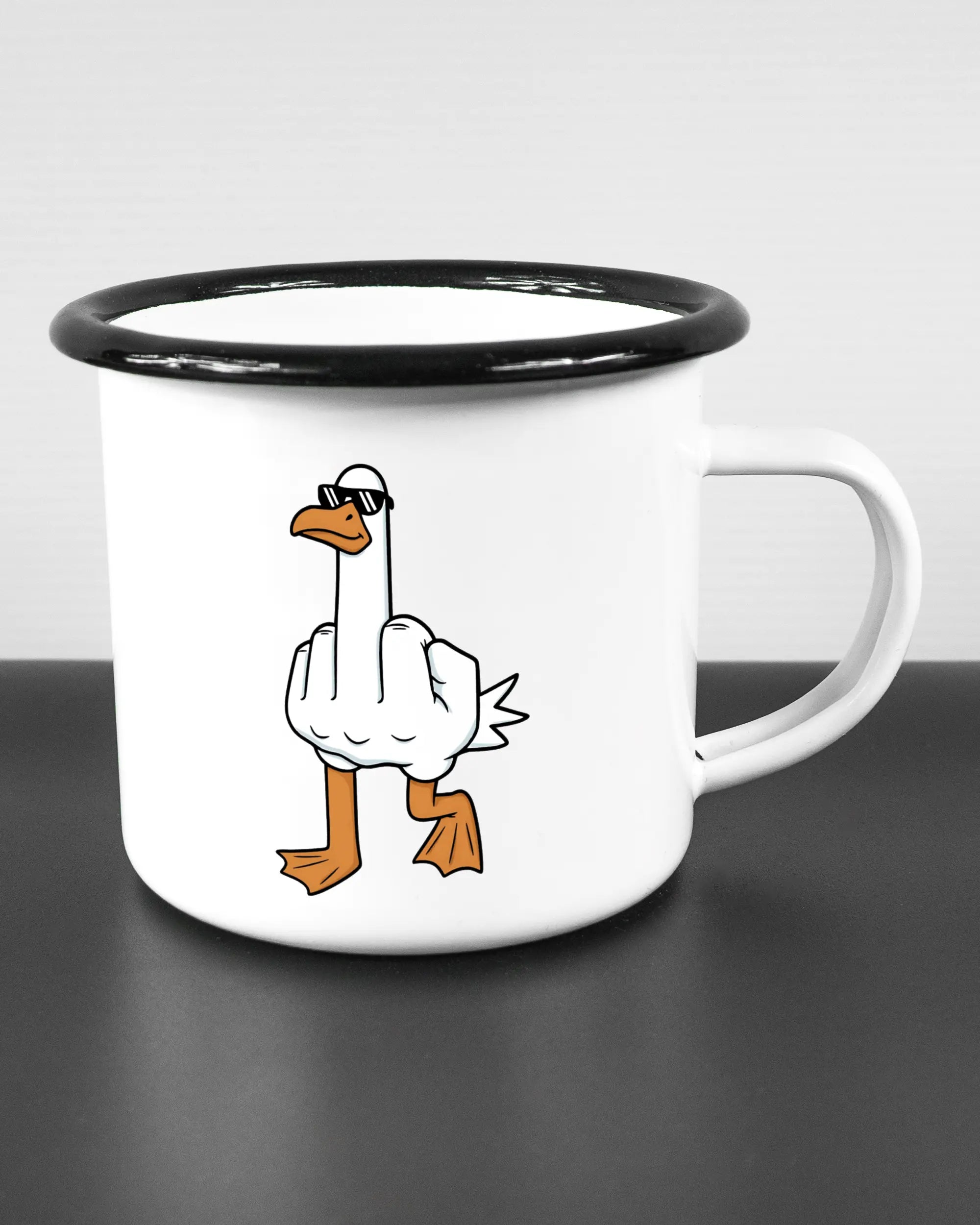 Alternativbild, das die rechte Seite der beidseitig bedruckten Emailletasse von Maondo mit dem Design I give a duck in der Farbe White-Black auf einem Holztisch zeigt