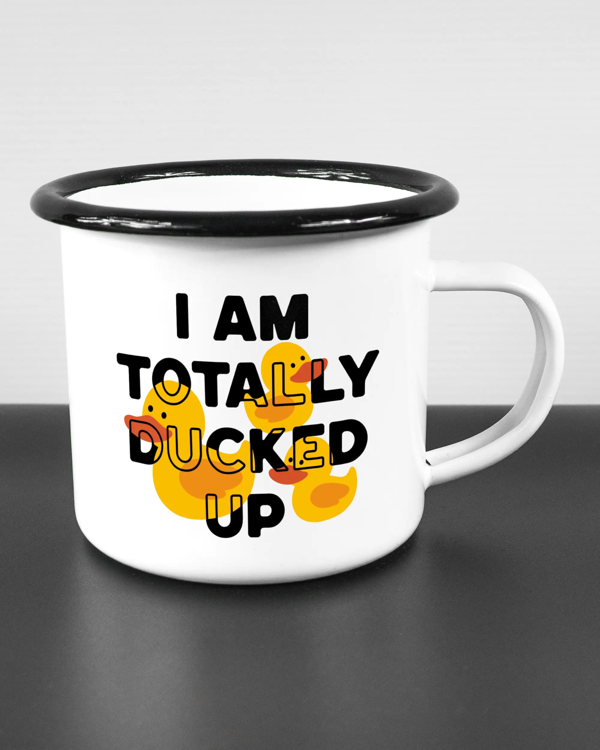 Alternativbild, das die rechte Seite der beidseitig bedruckten Emailletasse von Maondo mit dem Design Ducked Up in der Farbe White-Black auf einem Holztisch zeigt