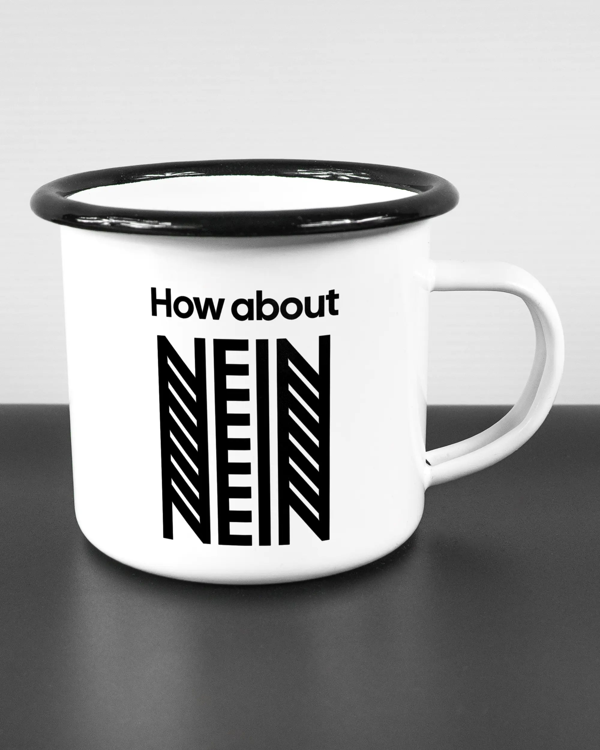 Alternativbild, das die rechte Seite der beidseitig bedruckten Emailletasse von Maondo mit dem Design How about nein in der Farbe White-Black auf einem Holztisch zeigt