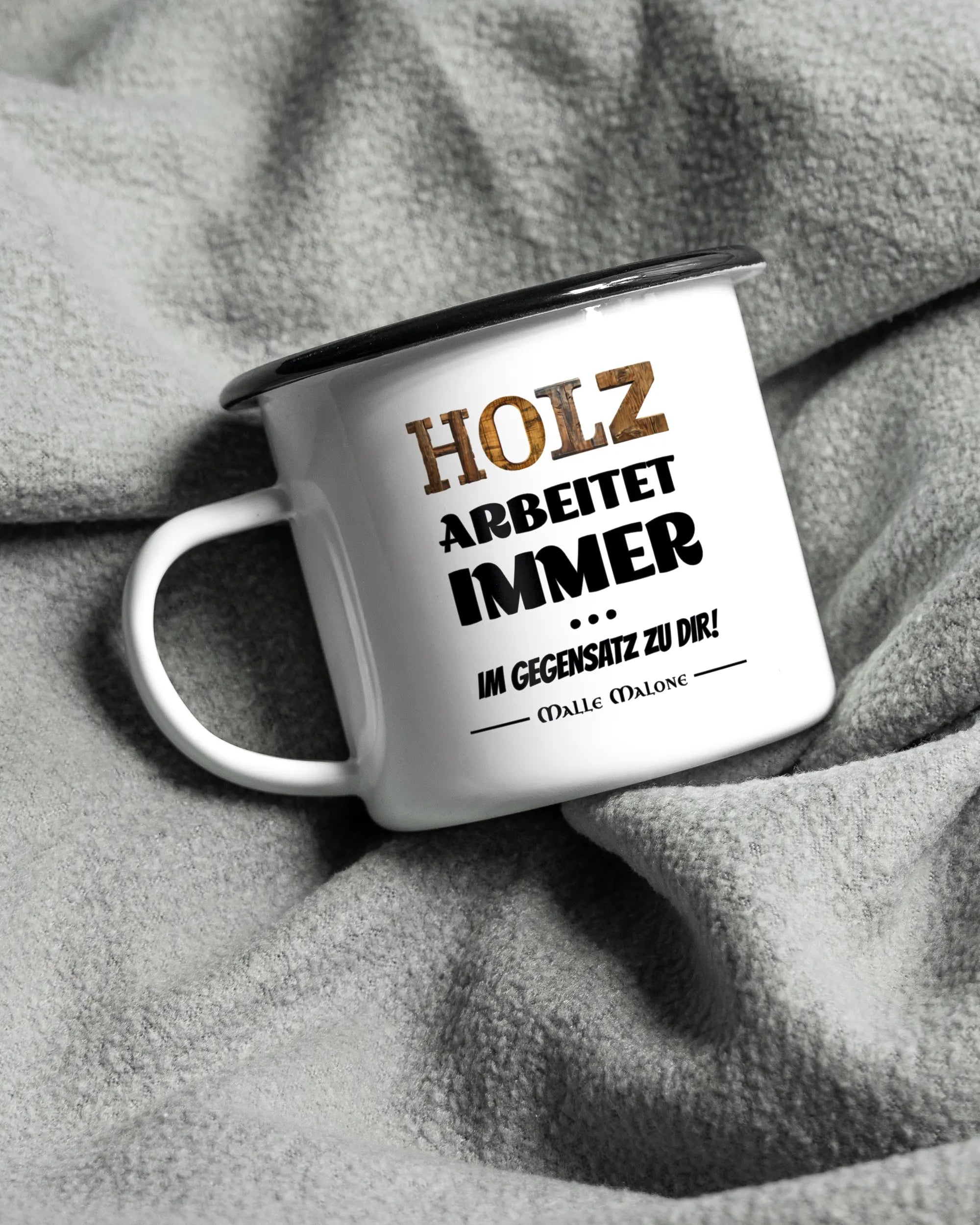 Aufnahme, die die linke Seite der beidseitig bedruckten Emailletasse von Maondo auf einer flauschigen Fließdecke mit dem Design Holzarbeit in der Farbe White-Black zeigt