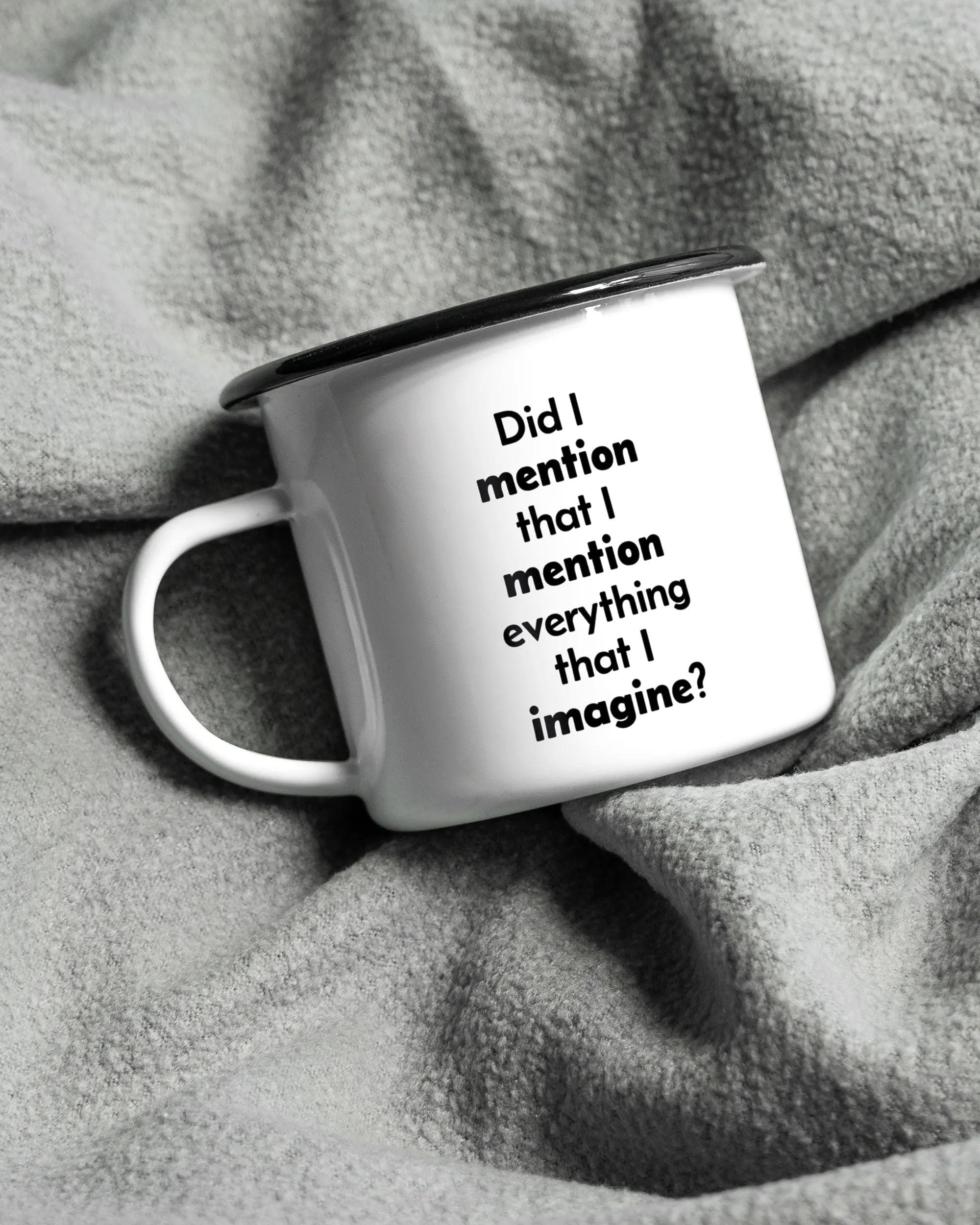 Aufnahme, die die linke Seite der beidseitig bedruckten Emailletasse von Maondo auf einer flauschigen Fließdecke mit dem Design Did I mention in der Farbe White-Black zeigt