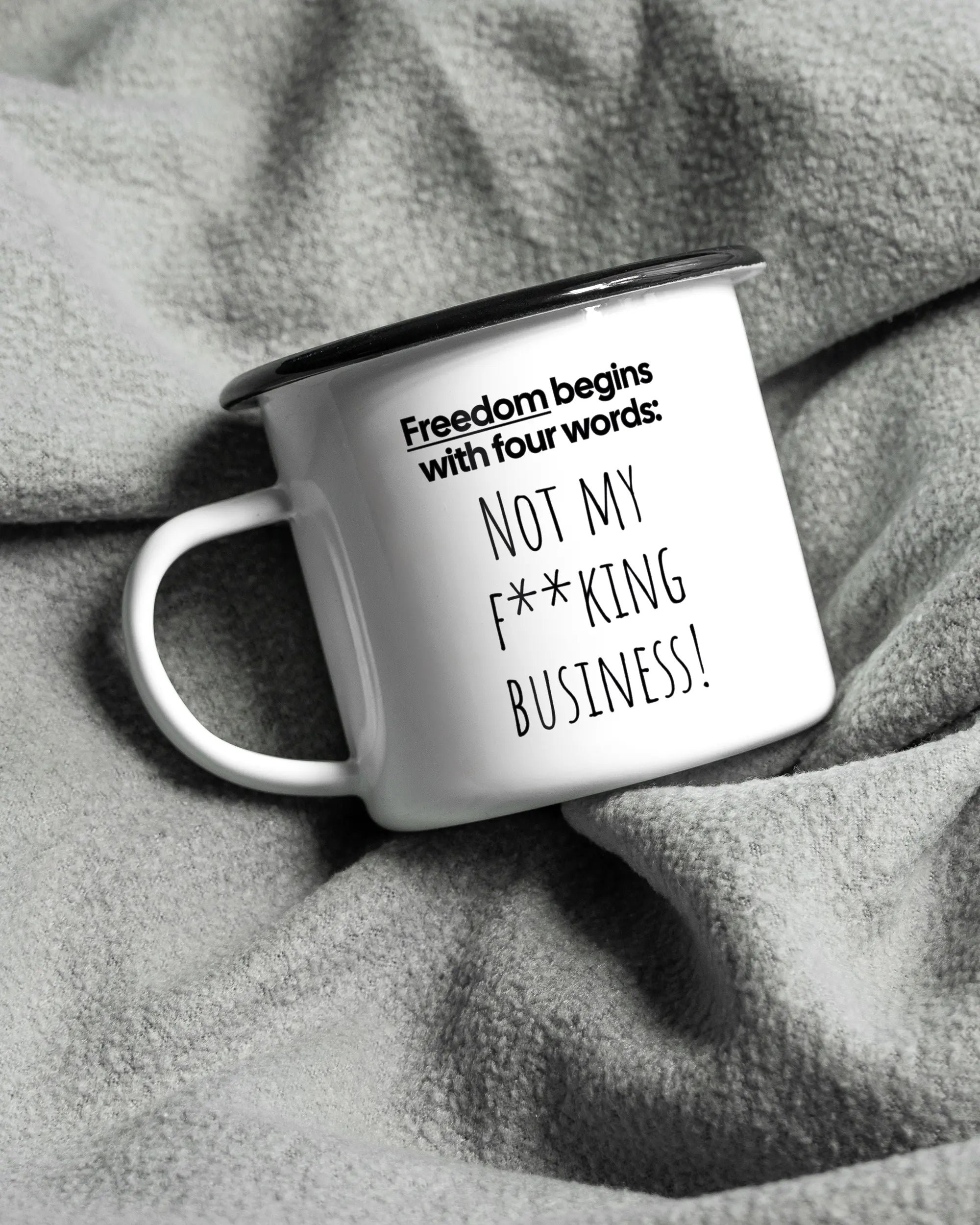 Aufnahme, die die linke Seite der beidseitig bedruckten Emailletasse von Maondo auf einer flauschigen Fließdecke mit dem Design 4 Freedom in der Farbe White-Black zeigt