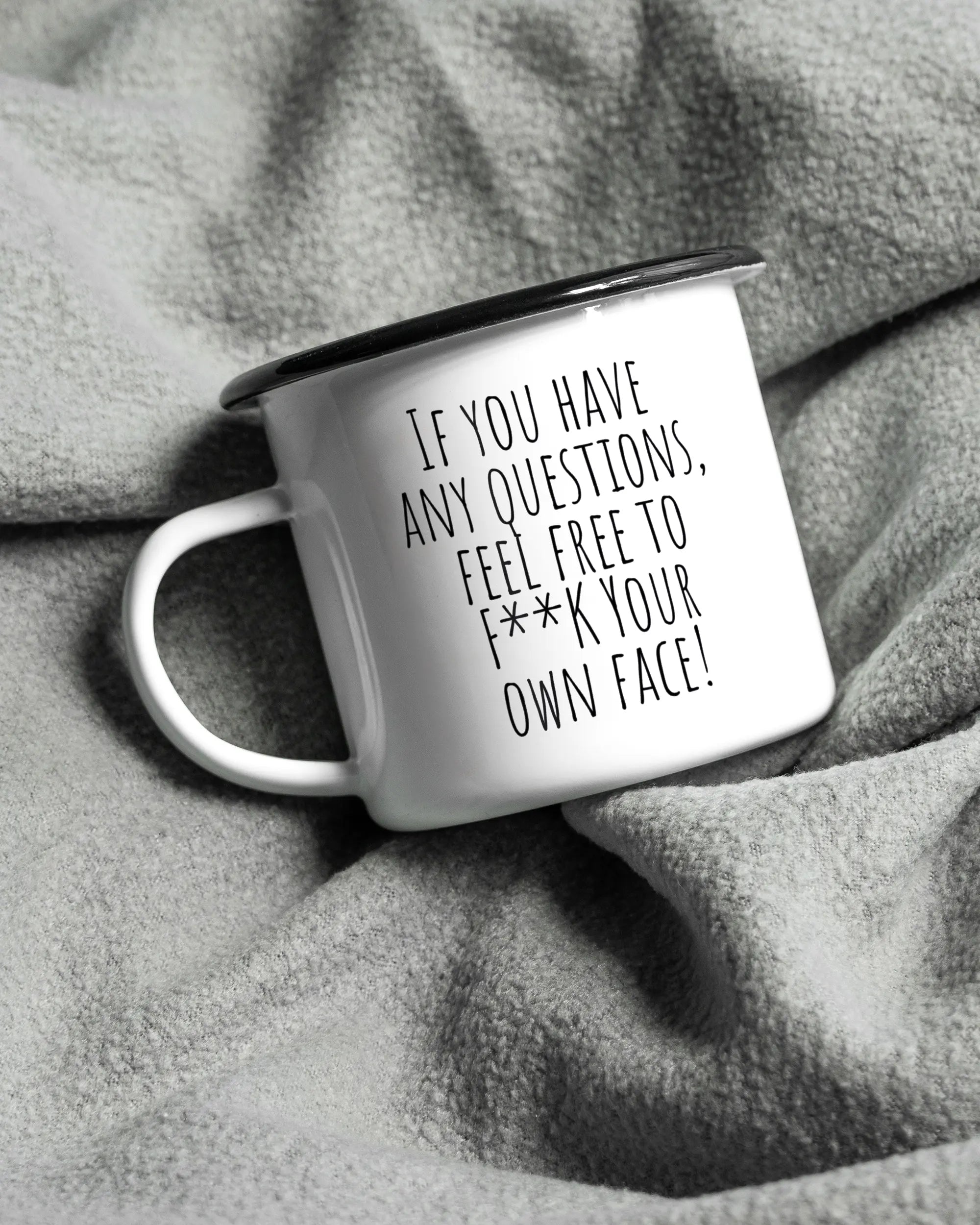 Aufnahme, die die linke Seite der beidseitig bedruckten Emailletasse von Maondo auf einer flauschigen Fließdecke mit dem Design Feel Free in der Farbe White-Black zeigt