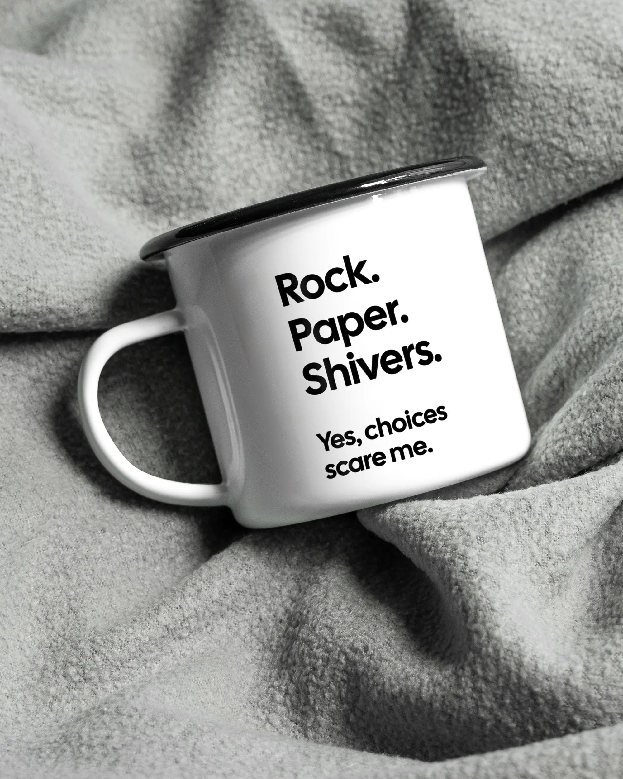 Aufnahme, die die linke Seite der beidseitig bedruckten Emailletasse von Maondo auf einer flauschigen Fließdecke mit dem Design Rock Paper Shivers in der Farbe White-Black zeigt