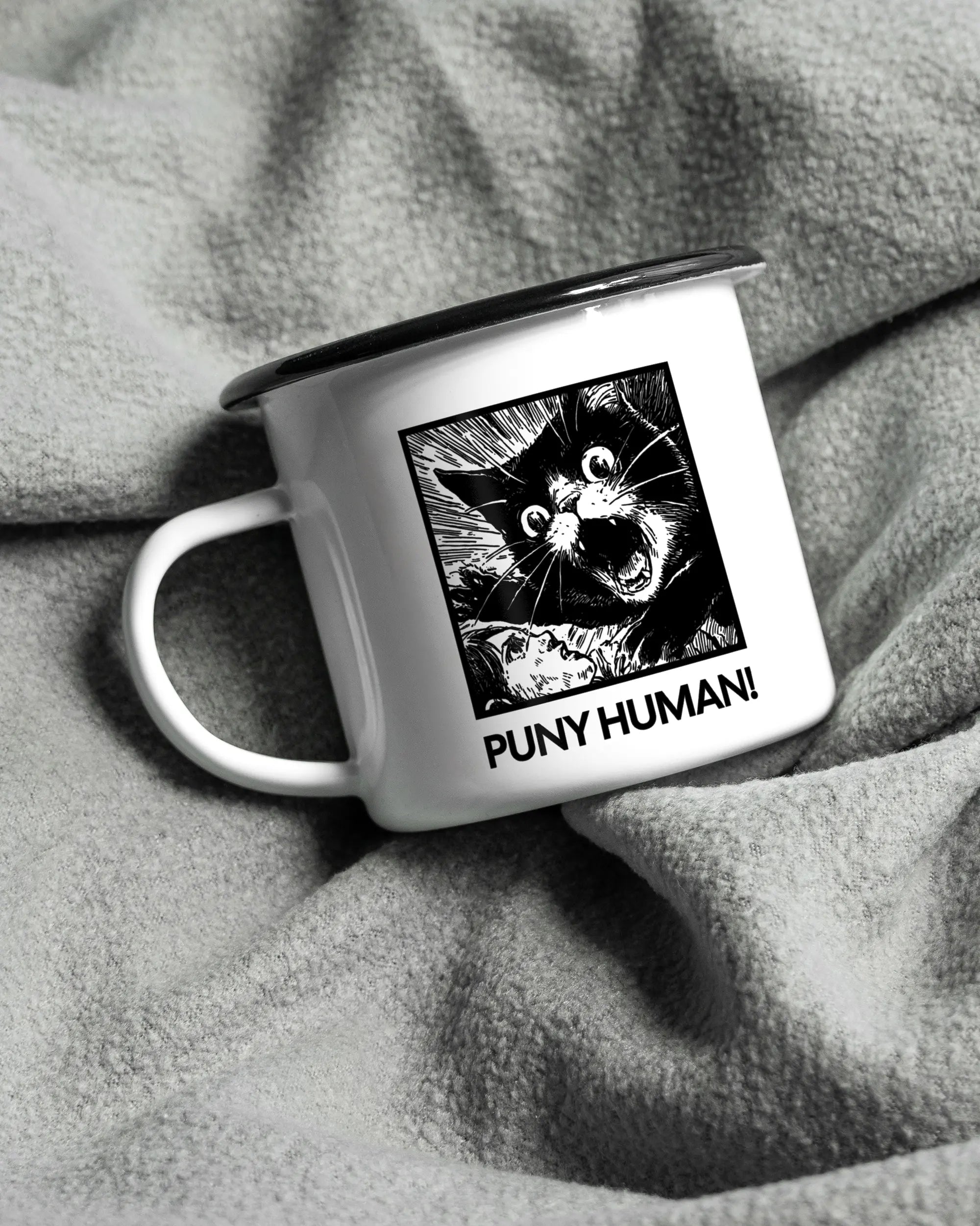 Aufnahme, die die linke Seite der beidseitig bedruckten Emailletasse von Maondo auf einer flauschigen Fließdecke mit dem Design Puny Human in der Farbe White-Black zeigt