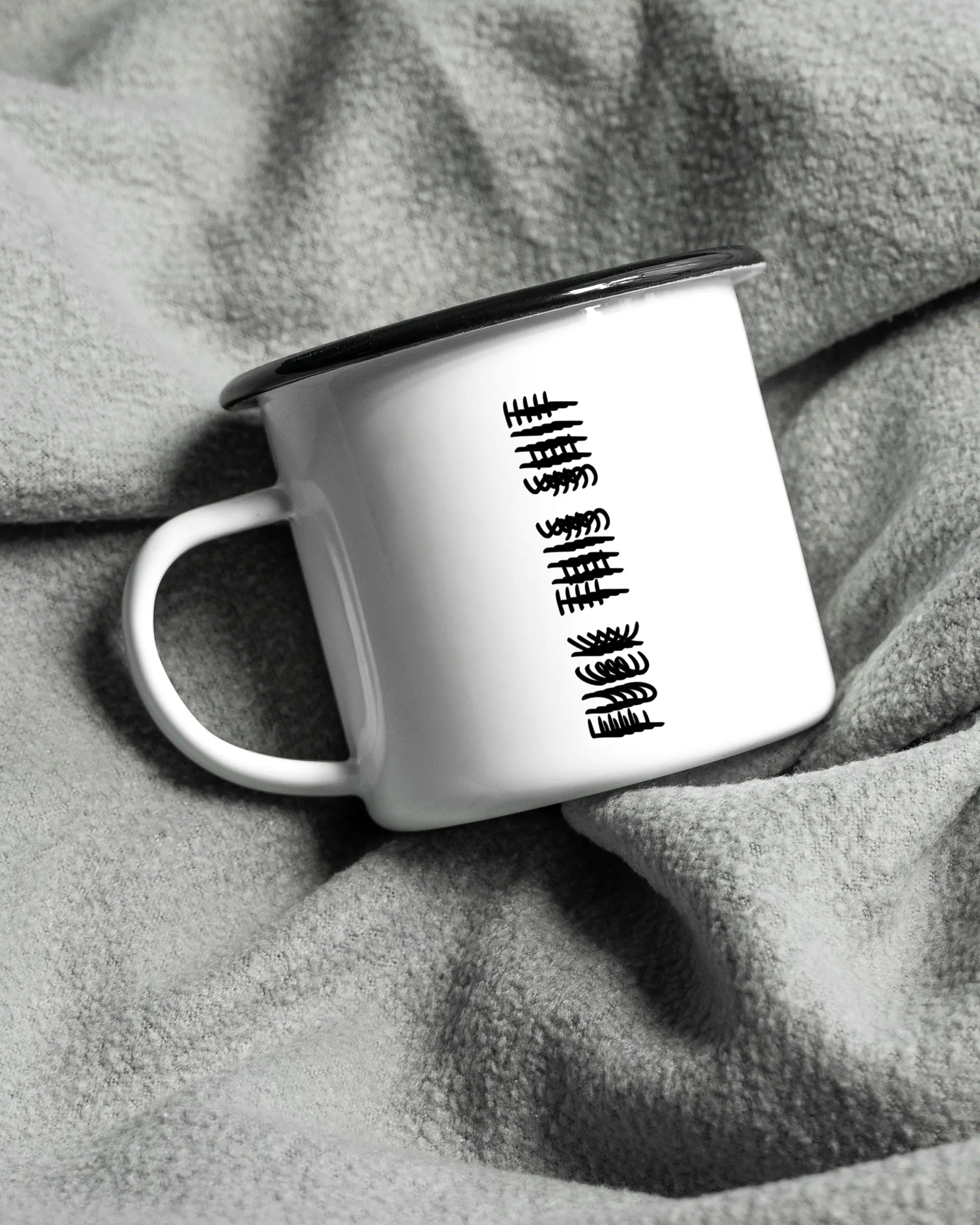 Aufnahme, die die linke Seite der beidseitig bedruckten Emailletasse von Maondo auf einer flauschigen Fließdecke mit dem Design Hidden Message in der Farbe White-Black zeigt