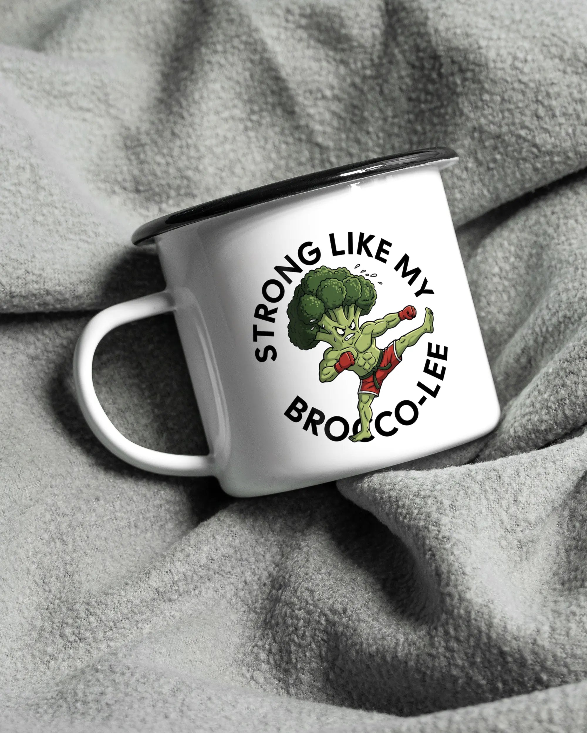 Aufnahme, die die linke Seite der beidseitig bedruckten Emailletasse von Maondo auf einer flauschigen Fließdecke mit dem Design Brocco-Lee in der Farbe White-Black zeigt