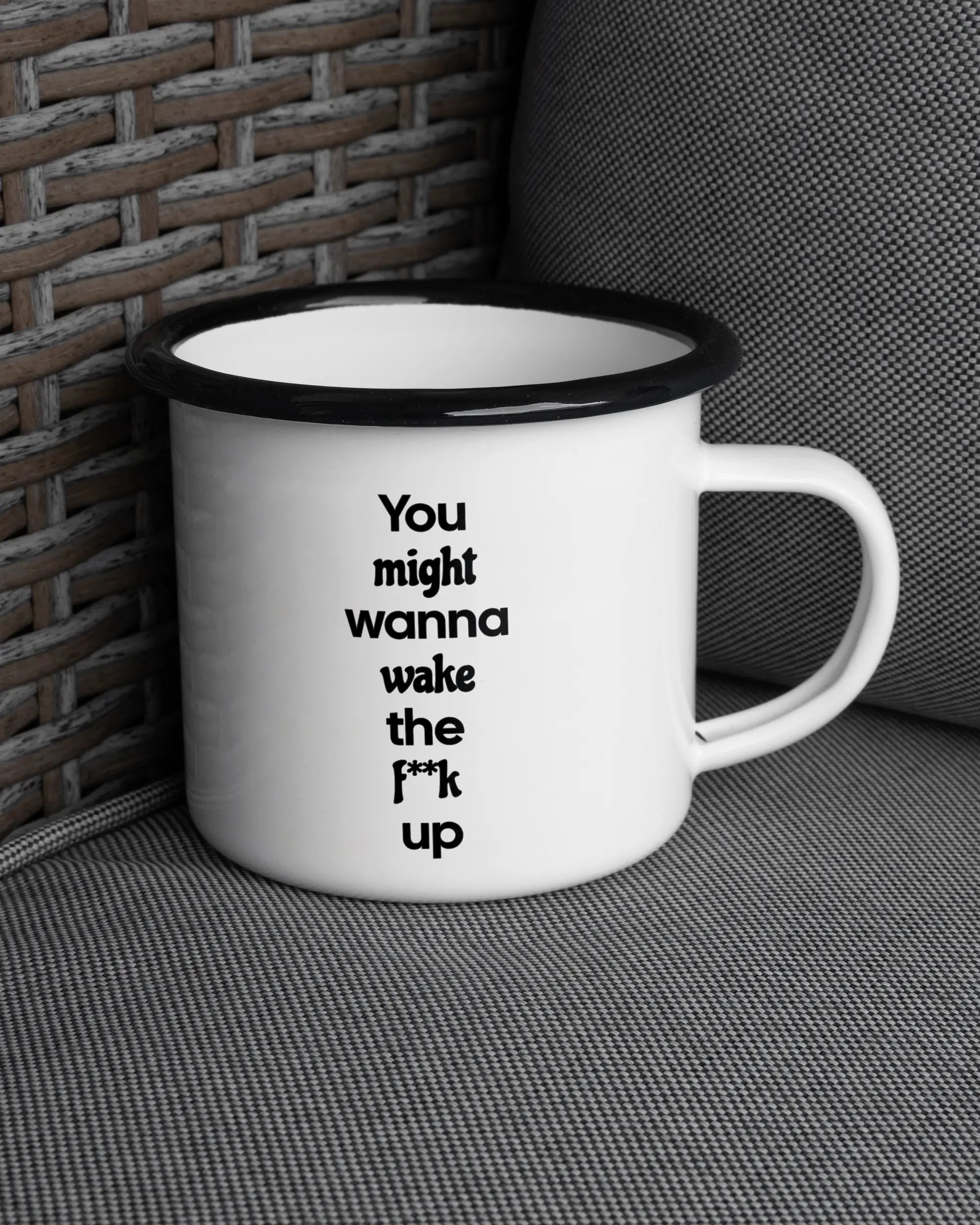 Ansicht der rechten Seite der beidseitig bedruckten Emailletasse von Maondo auf einem Balkonmöbel bzw. Campingstuhl mit dem Design Wanna Wake in der Farbe White-Black