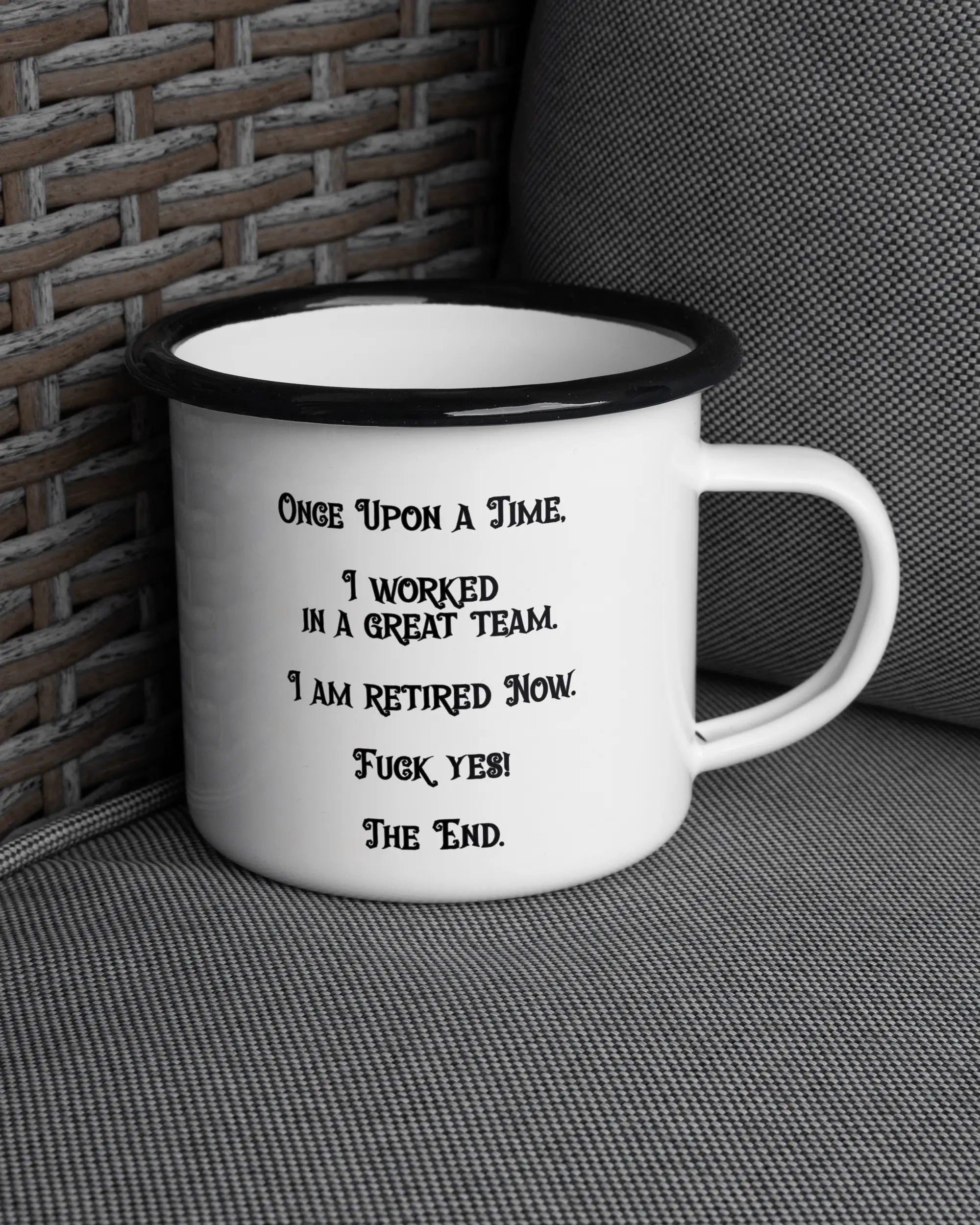 Ansicht der rechten Seite der beidseitig bedruckten Emailletasse von Maondo auf einem Balkonmöbel bzw. Campingstuhl mit dem Design Finally Retired in der Farbe White-Black