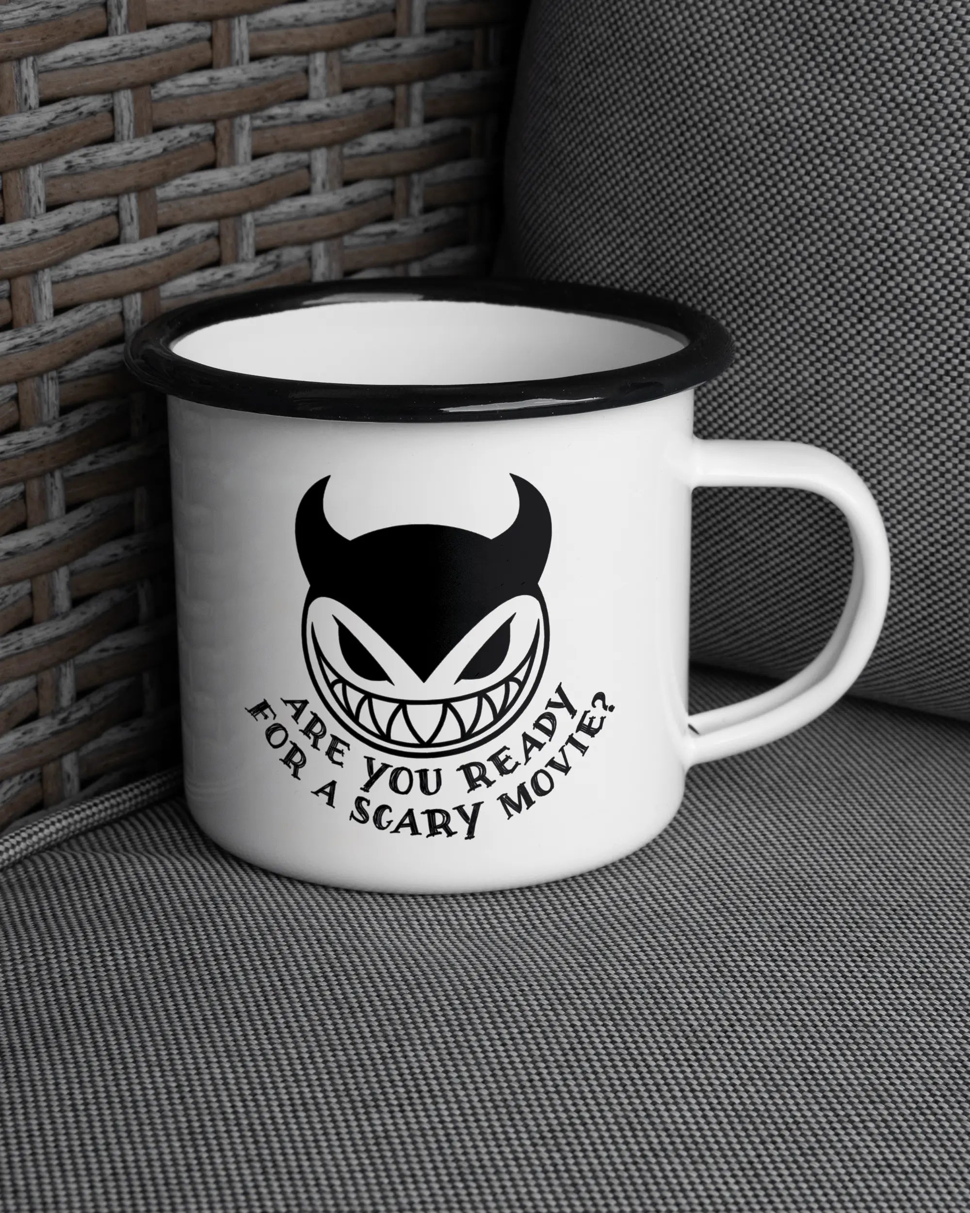 Ansicht der rechten Seite der beidseitig bedruckten Emailletasse von Maondo auf einem Balkonmöbel bzw. Campingstuhl mit dem Design Scary Movie in der Farbe White-Black