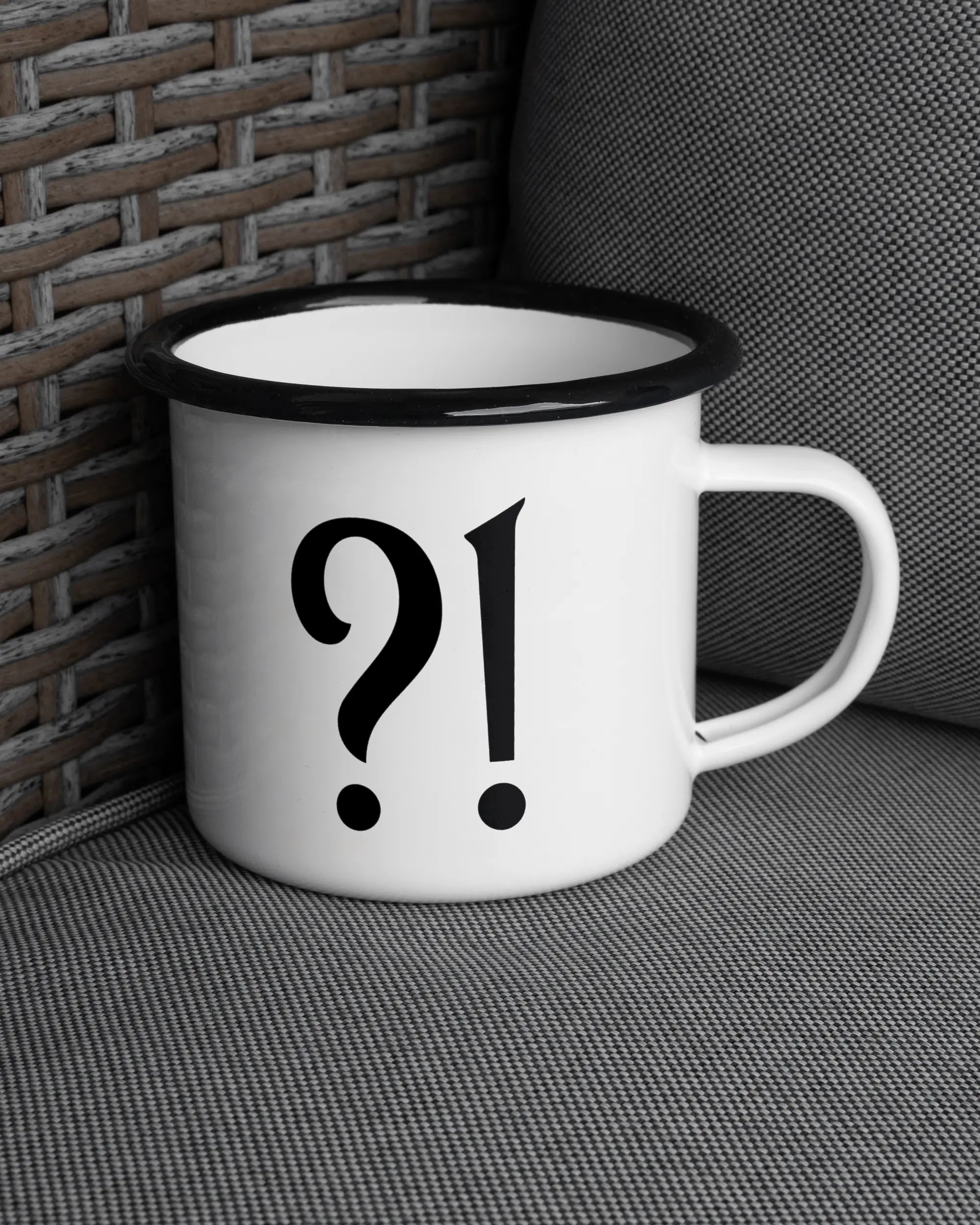 Ansicht der rechten Seite der beidseitig bedruckten Emailletasse von Maondo auf einem Balkonmöbel bzw. Campingstuhl mit dem Design WHAT in der Farbe White-Black