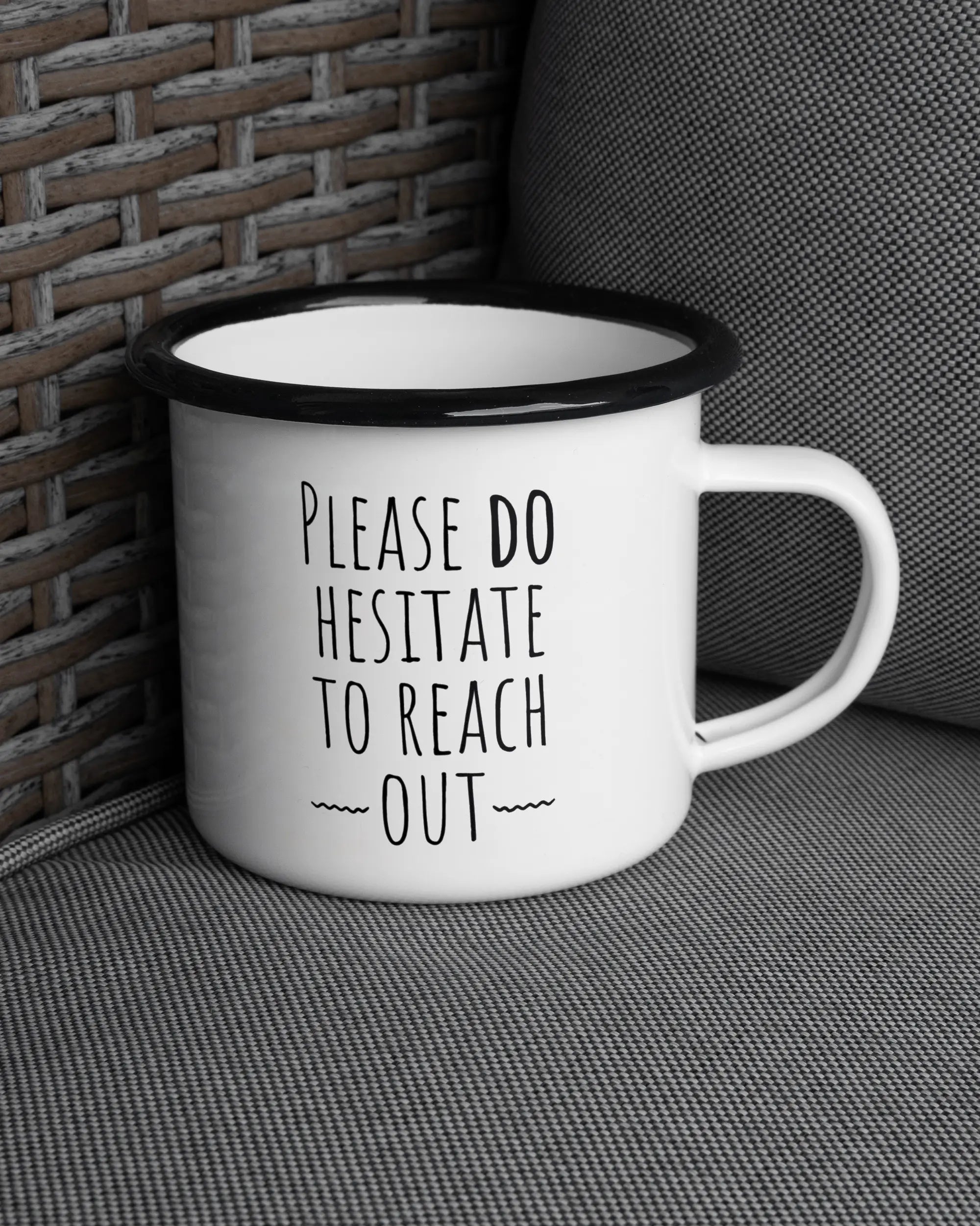 Ansicht der rechten Seite der beidseitig bedruckten Emailletasse von Maondo auf einem Balkonmöbel bzw. Campingstuhl mit dem Design Please Hesitate in der Farbe White-Black