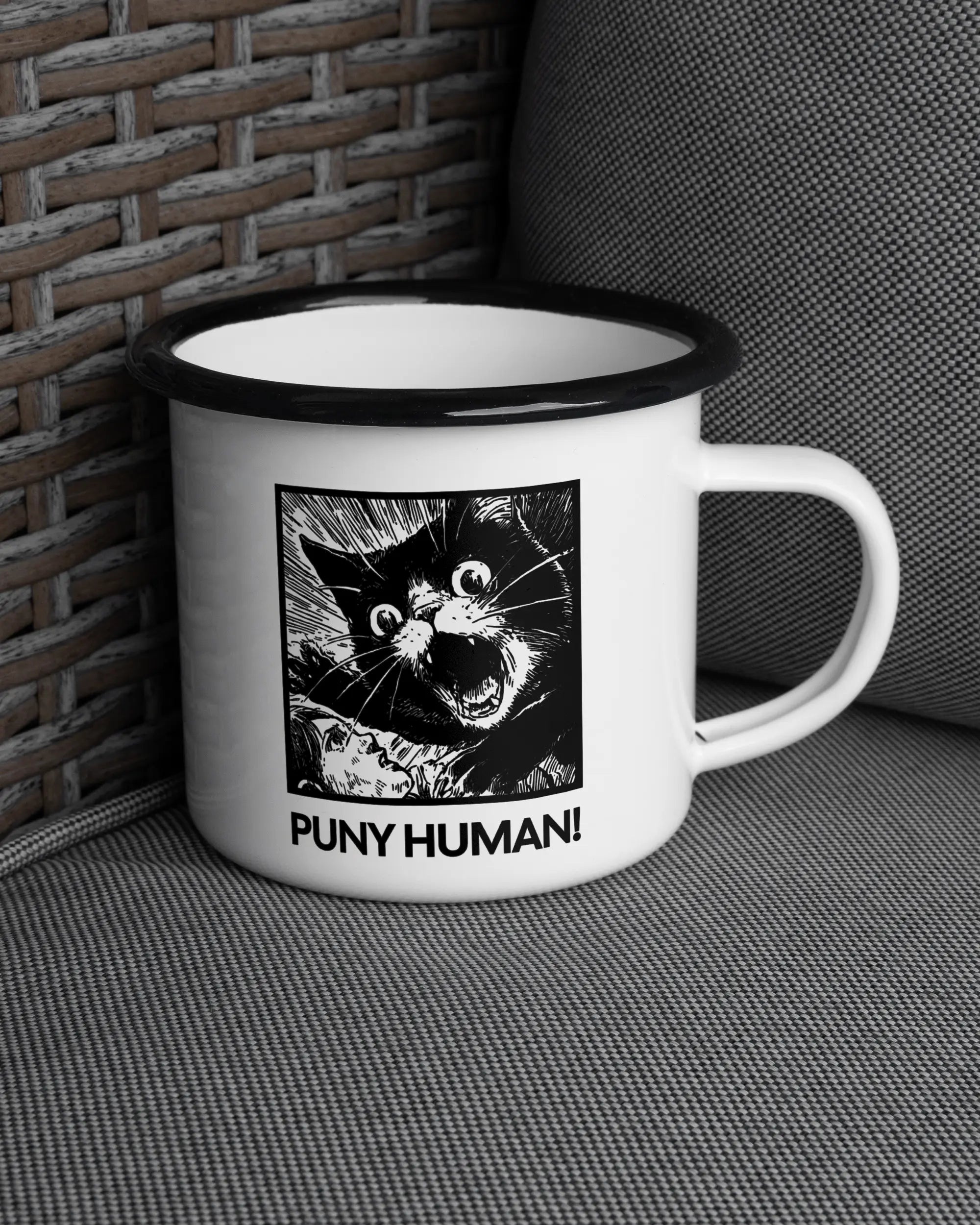Ansicht der rechten Seite der beidseitig bedruckten Emailletasse von Maondo auf einem Balkonmöbel bzw. Campingstuhl mit dem Design Puny Human in der Farbe White-Black