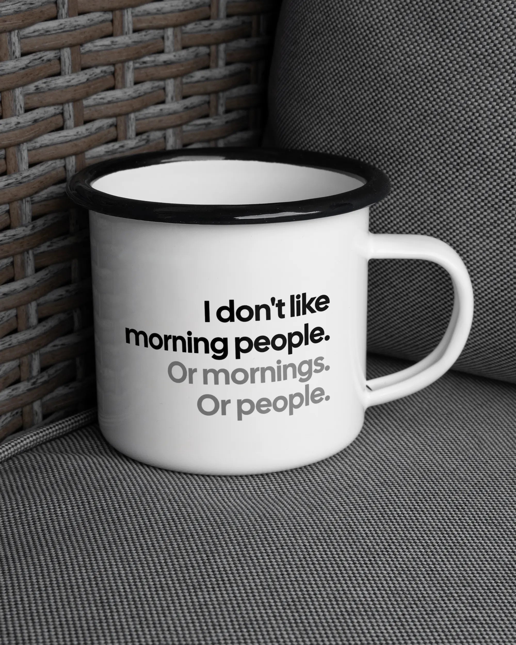 Ansicht der rechten Seite der beidseitig bedruckten Emailletasse von Maondo auf einem Balkonmöbel bzw. Campingstuhl mit dem Design Morning Person in der Farbe White-Black