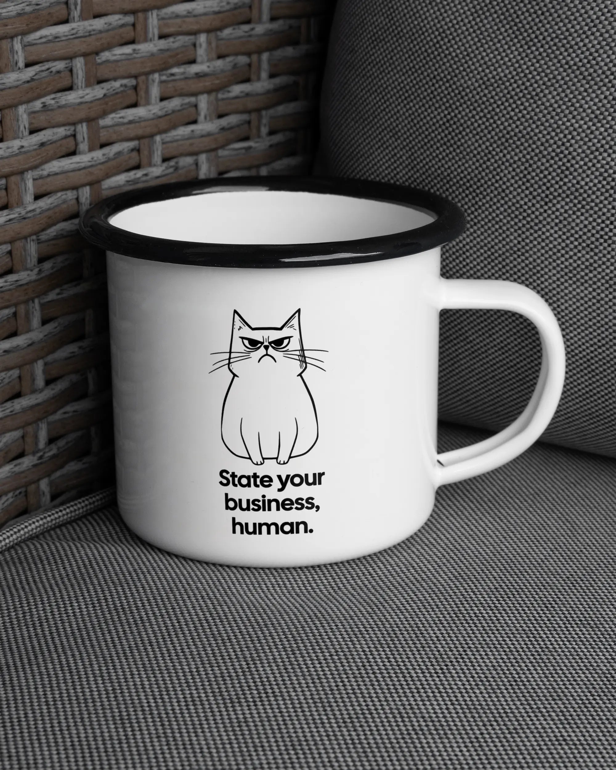 Ansicht der rechten Seite der beidseitig bedruckten Emailletasse von Maondo auf einem Balkonmöbel bzw. Campingstuhl mit dem Design Grumpy Purr in der Farbe White-Black