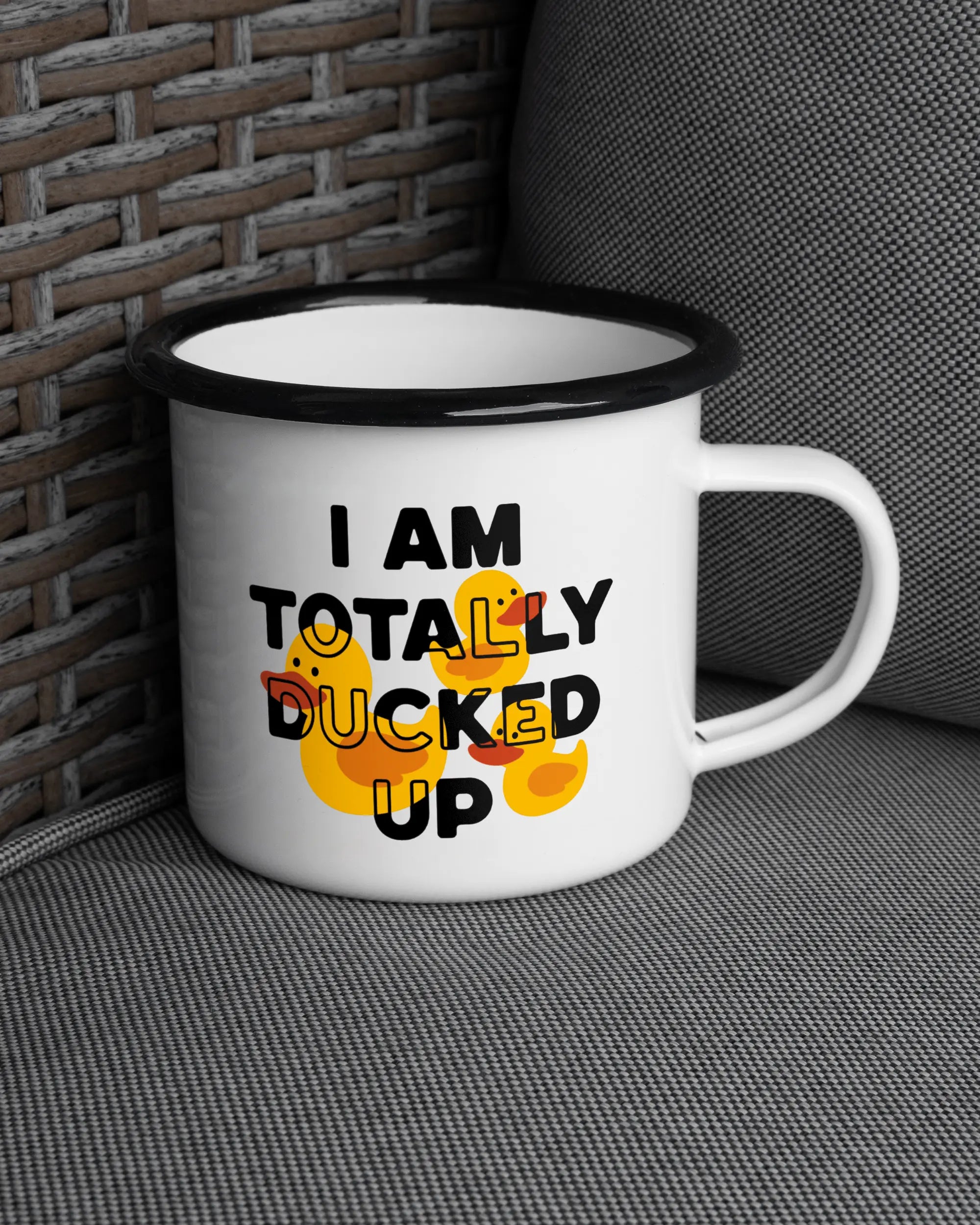 Ansicht der rechten Seite der beidseitig bedruckten Emailletasse von Maondo auf einem Balkonmöbel bzw. Campingstuhl mit dem Design Ducked Up in der Farbe White-Black