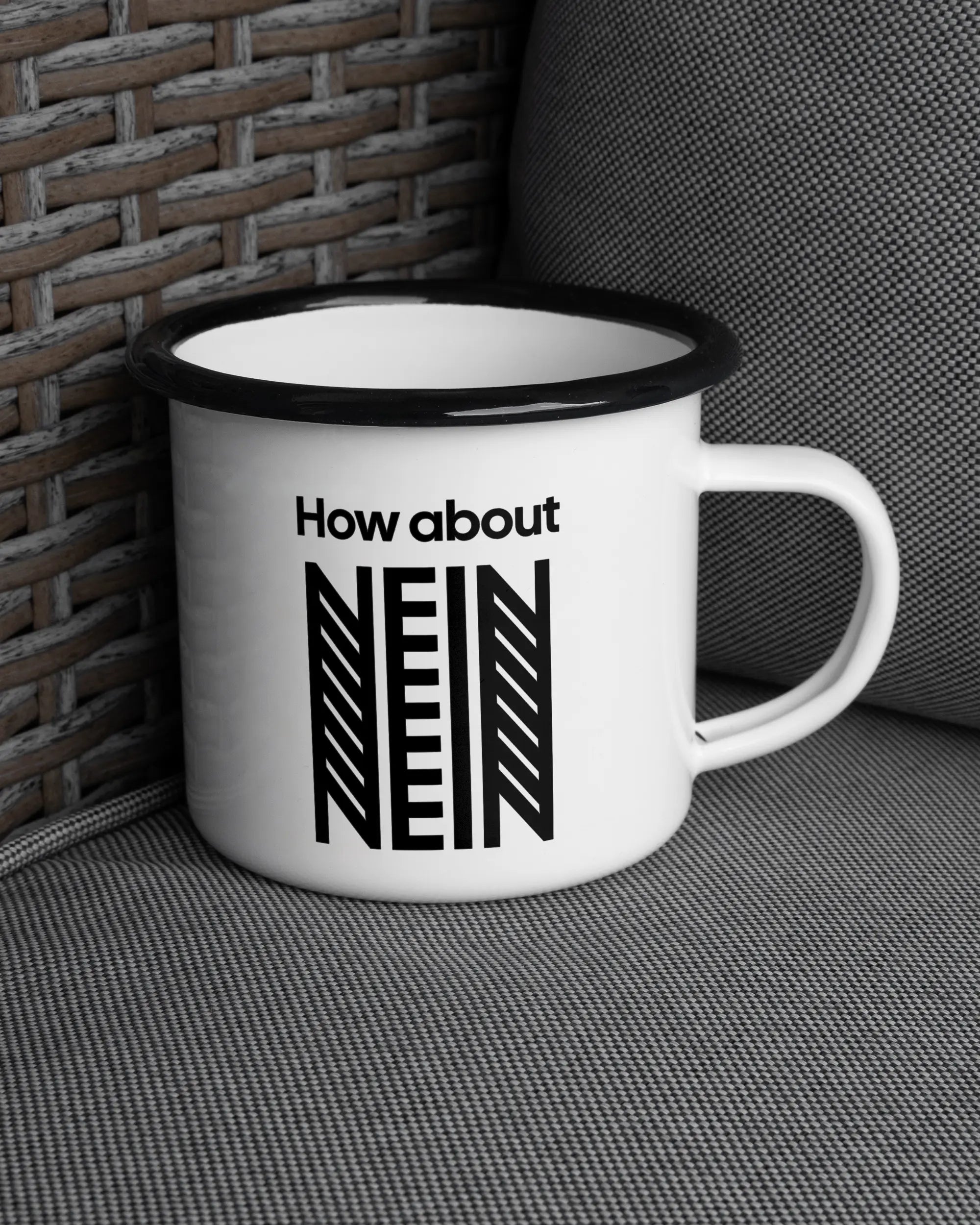 Ansicht der rechten Seite der beidseitig bedruckten Emailletasse von Maondo auf einem Balkonmöbel bzw. Campingstuhl mit dem Design How about nein in der Farbe White-Black