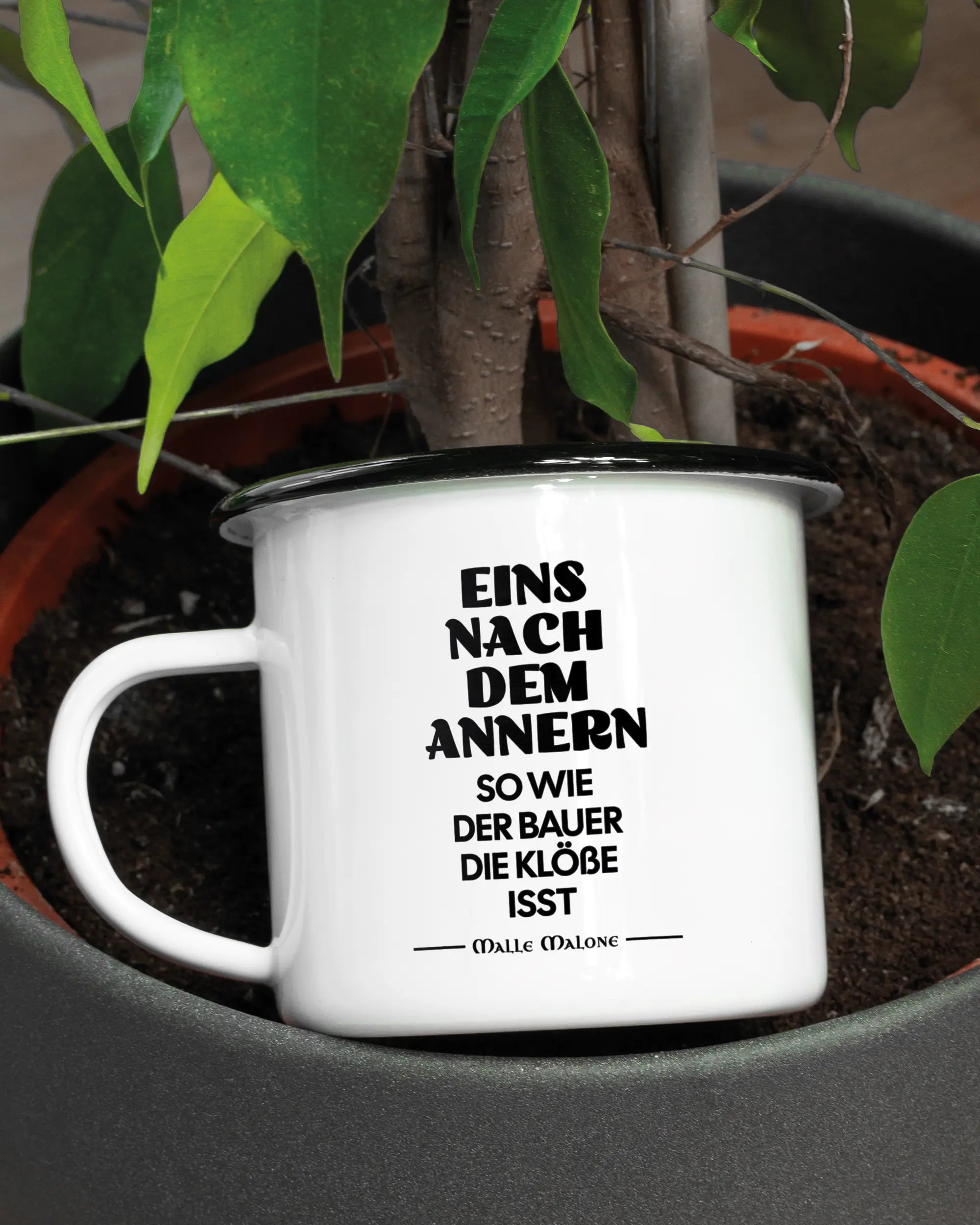 Aufnahme der linken Seite der beidseitig bedruckten Emailletasse von Maondo mit dem Design Eins nach dem Annern in der Farbe White-Black in einem Blumentopf