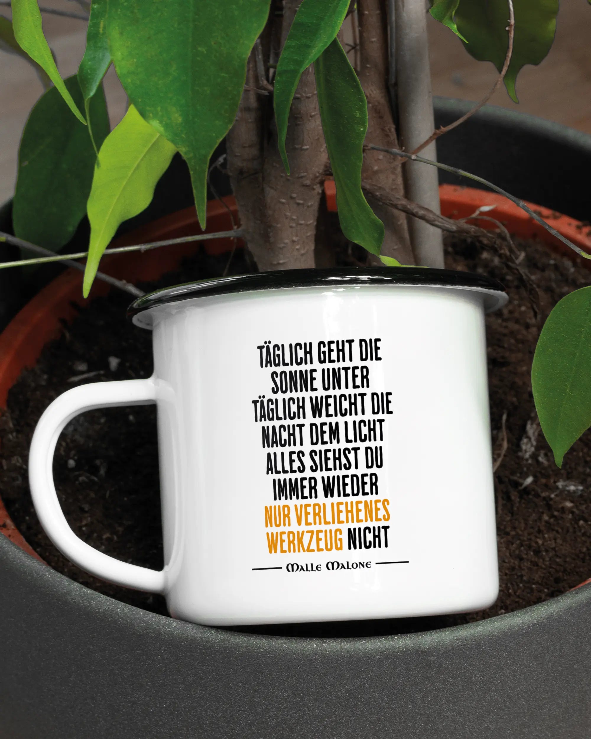Aufnahme der linken Seite der beidseitig bedruckten Emailletasse von Maondo mit dem Design Wegzeug in der Farbe White-Black in einem Blumentopf