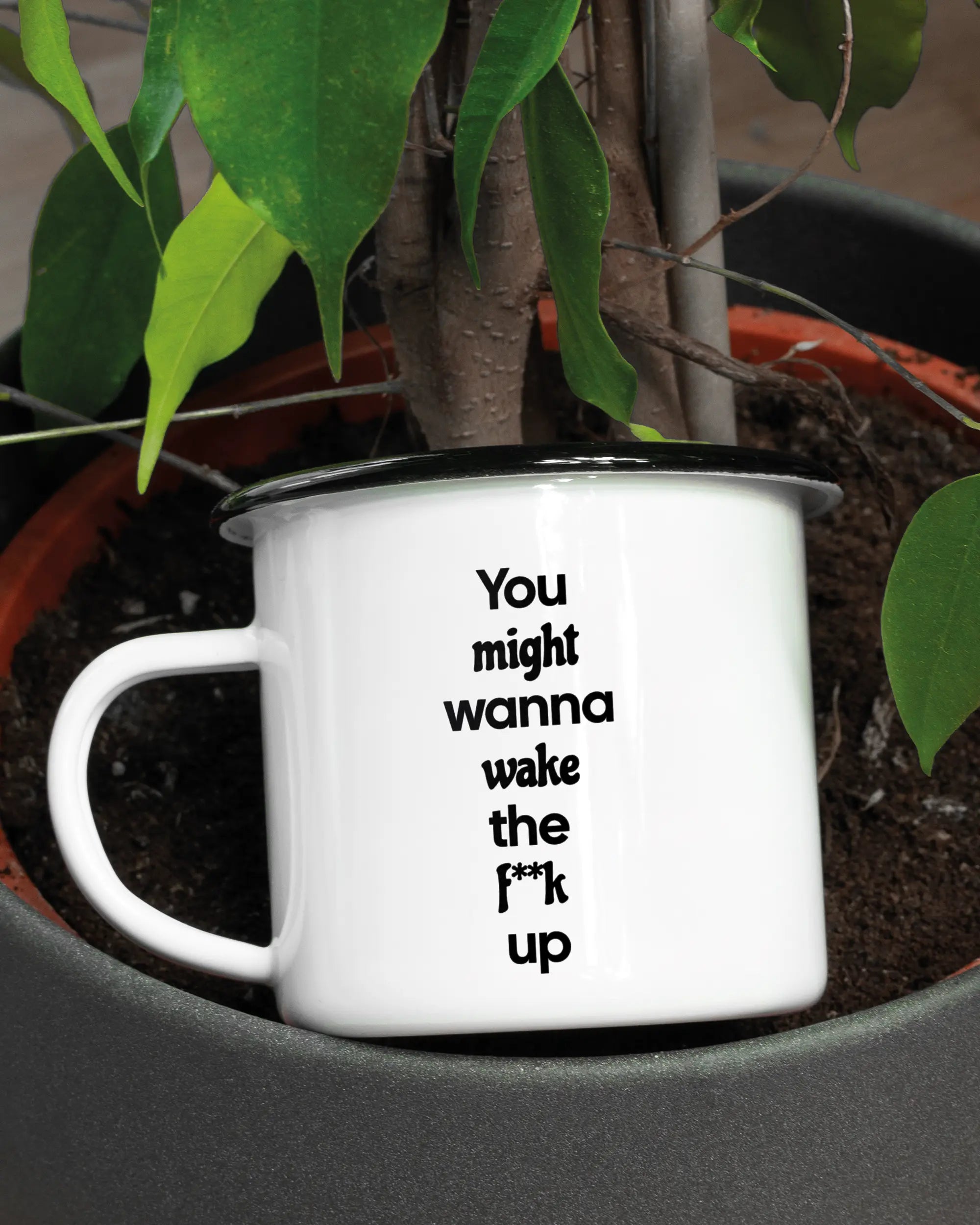 Aufnahme der linken Seite der beidseitig bedruckten Emailletasse von Maondo mit dem Design Wanna Wake in der Farbe White-Black in einem Blumentopf