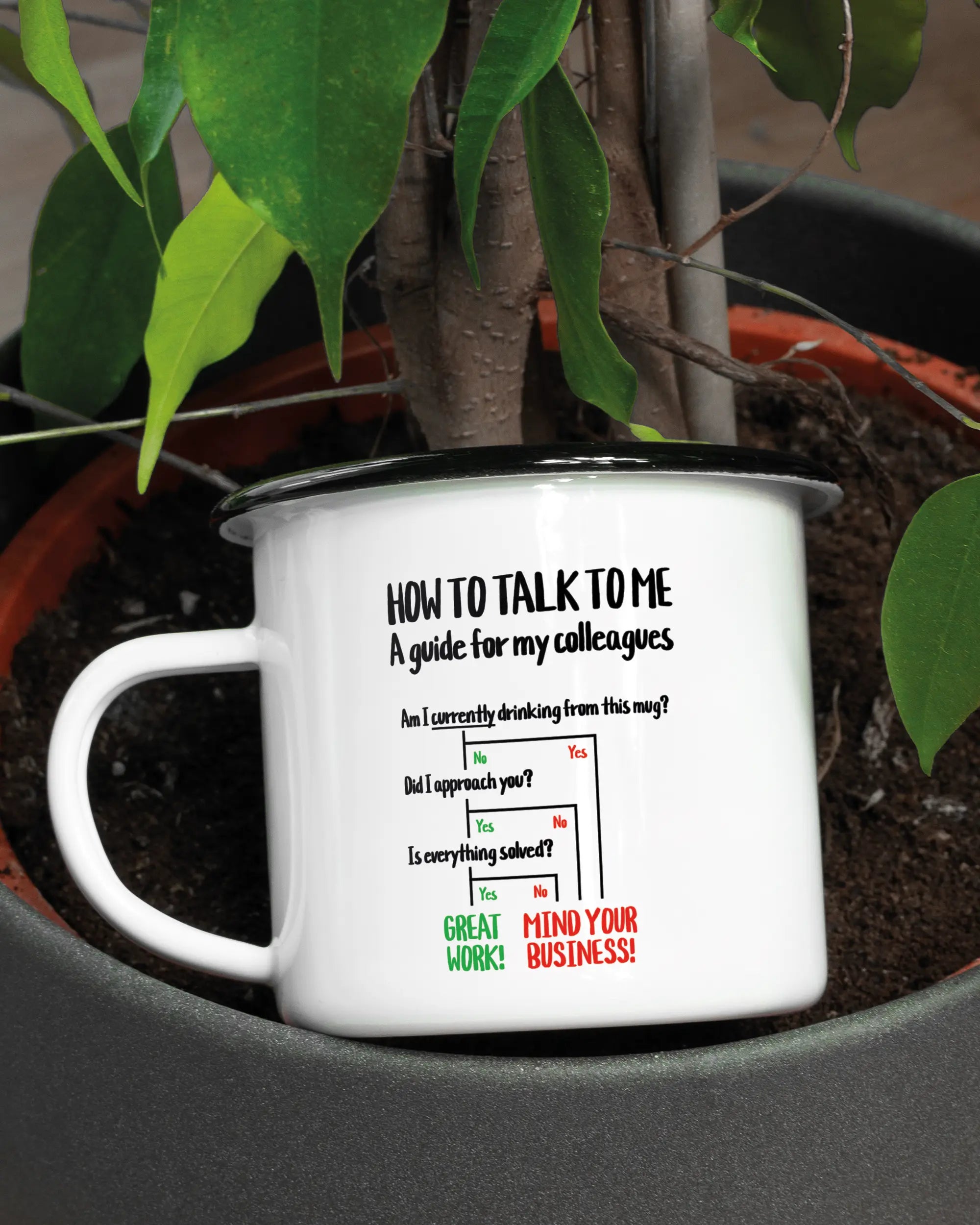 Aufnahme der linken Seite der beidseitig bedruckten Emailletasse von Maondo mit dem Design Colleagues Guide in der Farbe White-Black in einem Blumentopf