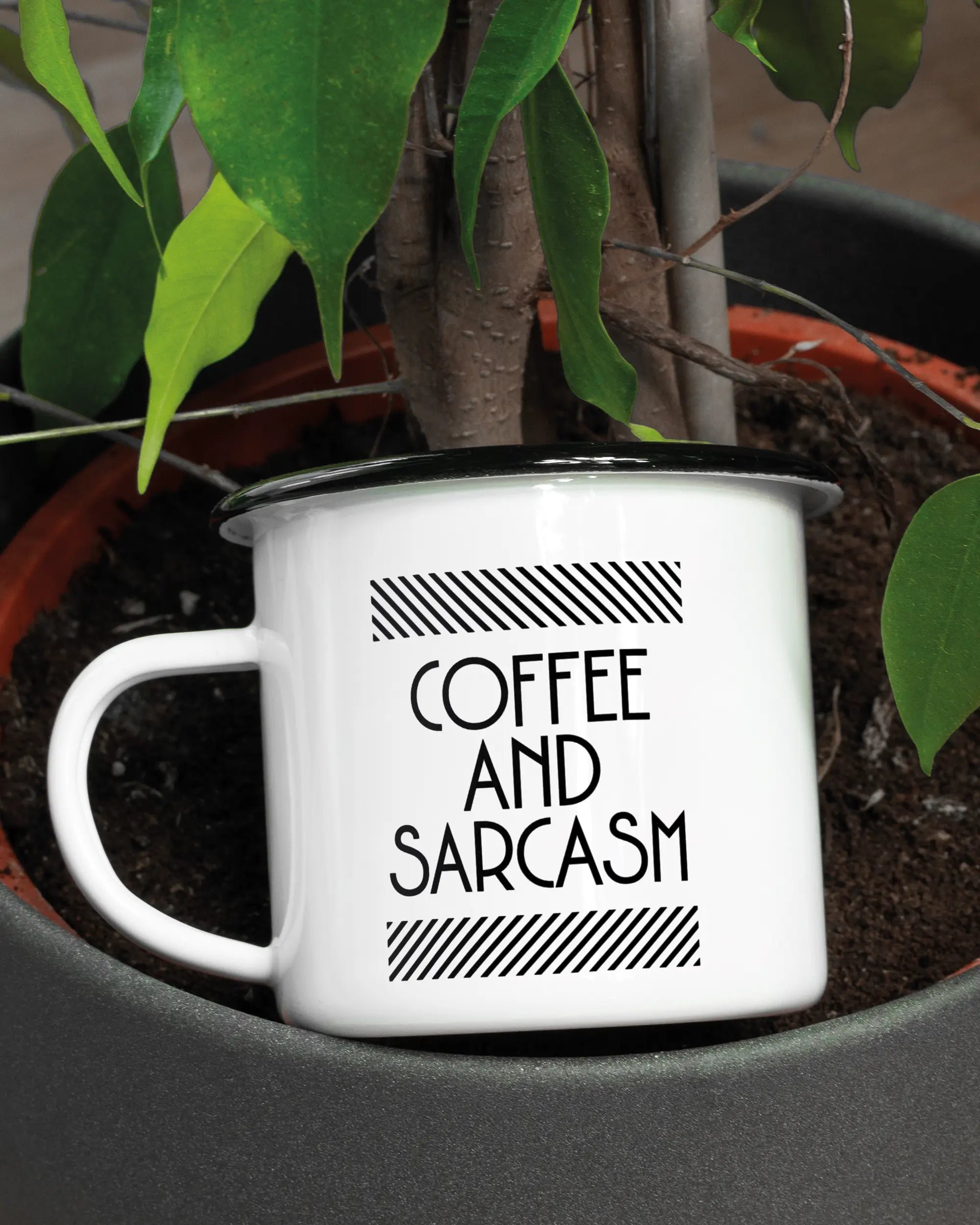 Aufnahme der linken Seite der beidseitig bedruckten Emailletasse von Maondo mit dem Design Sarcastic Cup in der Farbe White-Black in einem Blumentopf