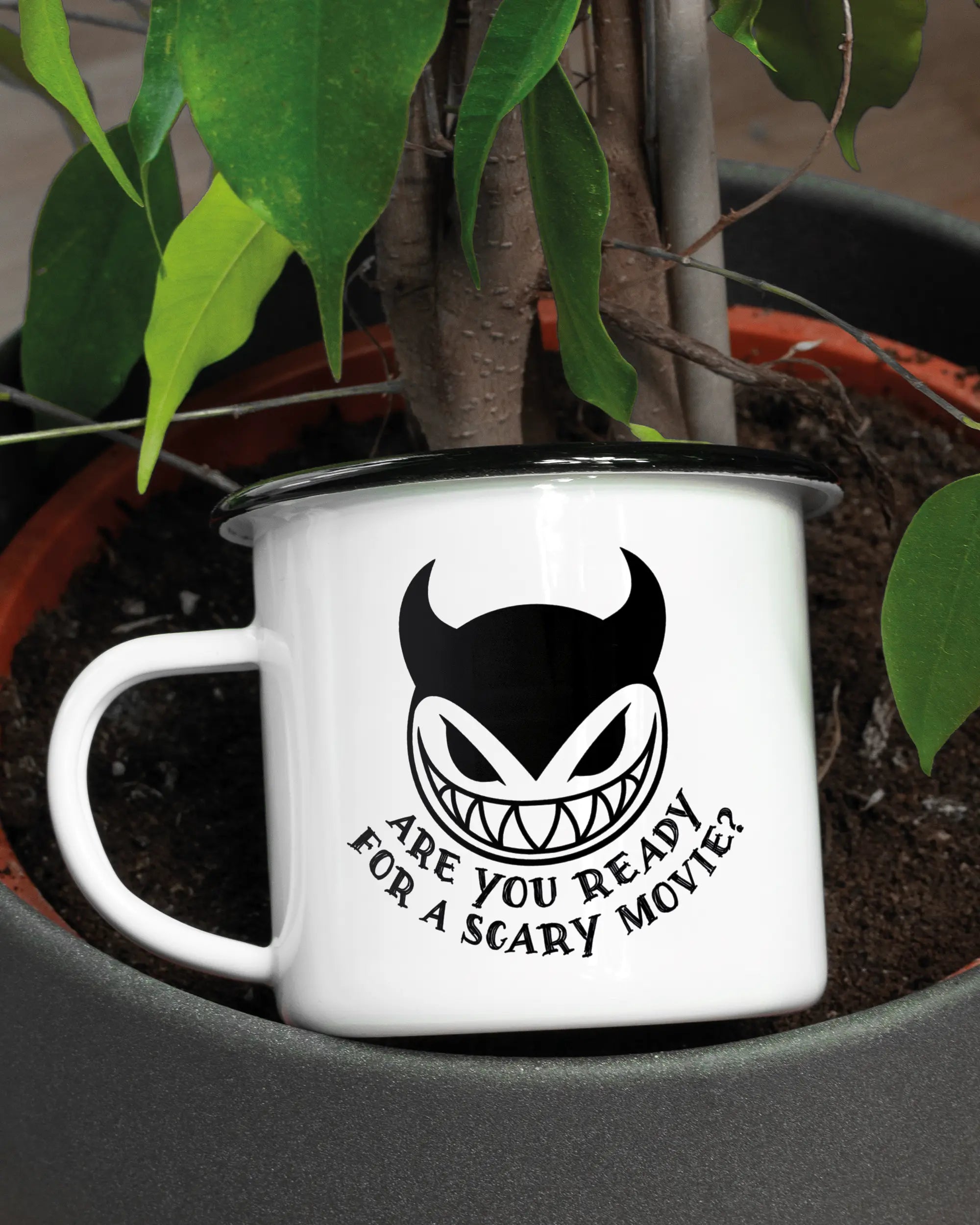 Aufnahme der linken Seite der beidseitig bedruckten Emailletasse von Maondo mit dem Design Scary Movie in der Farbe White-Black in einem Blumentopf