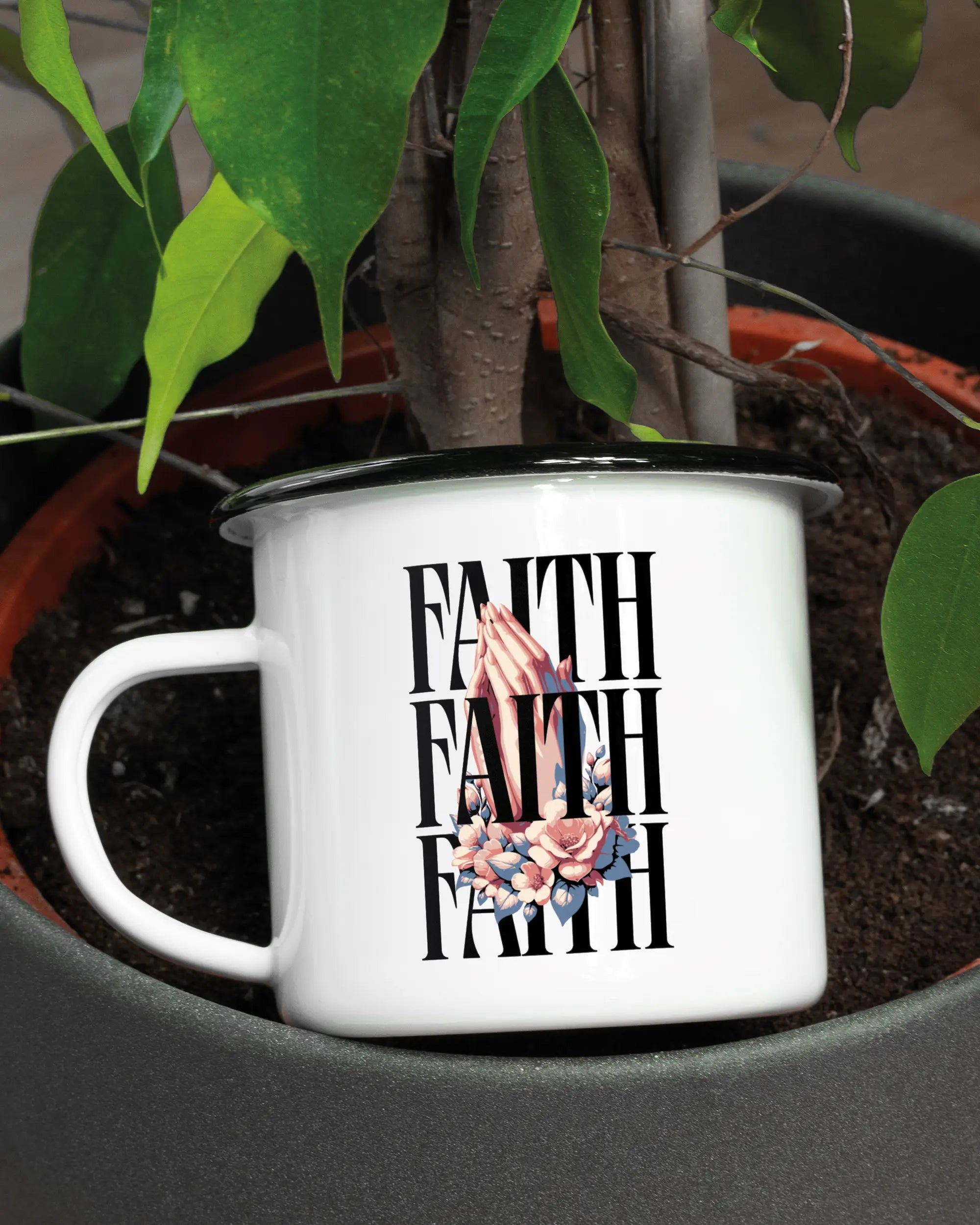 Aufnahme der linken Seite der beidseitig bedruckten Emailletasse von Maondo mit dem Design Faith X3 in der Farbe White-Black in einem Blumentopf